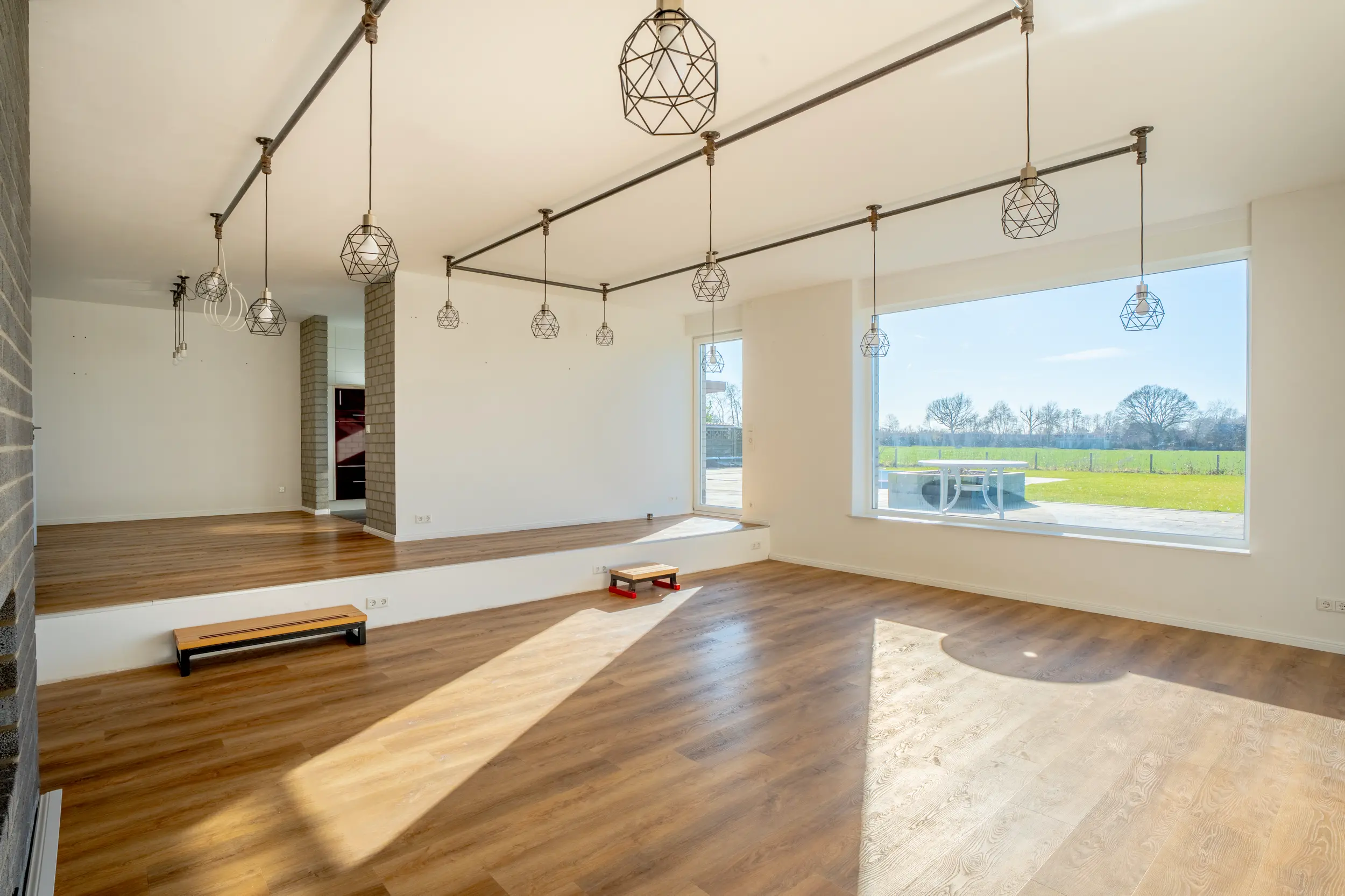 Lichtdurchflutetes Wohnzimmer mit großem Panoramafenster, Eichenparkett und modernen geometrischen Pendelleuchten mit Blick ins Grüne