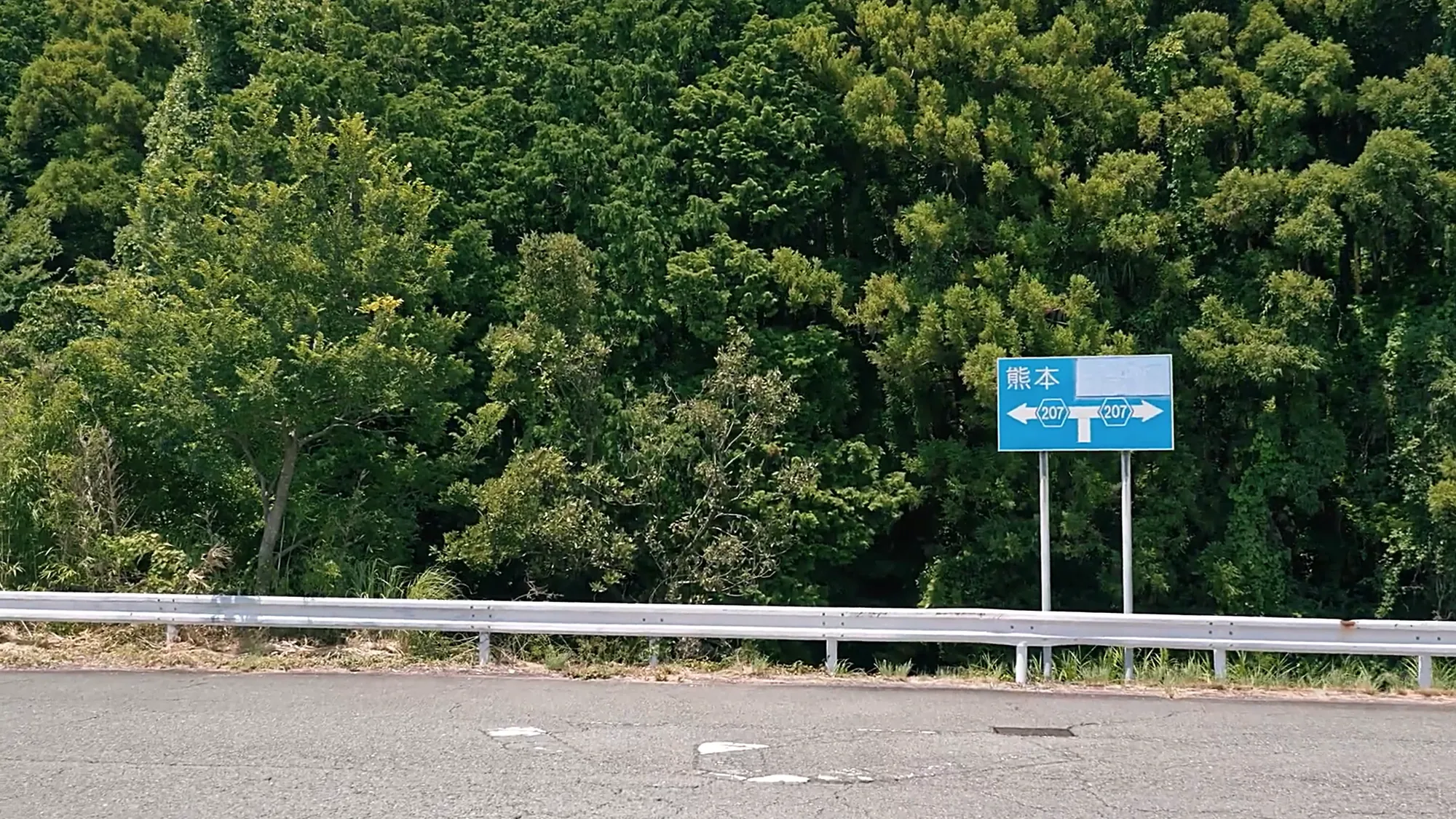 A caldera road near Kurokawa Onsen with a blue direction sign for Kumamoto