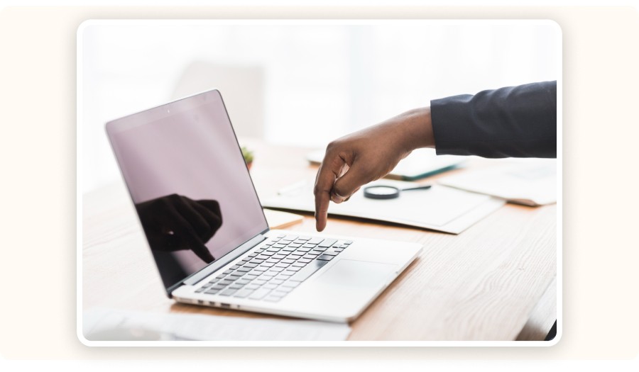 Hand pointing at laptop screen on desk