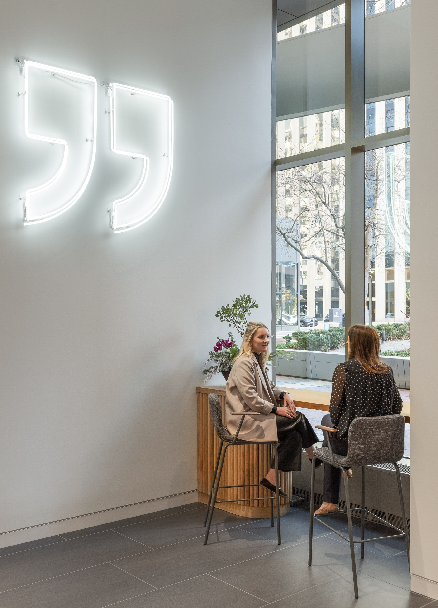 Neon quotation marks above two women talking