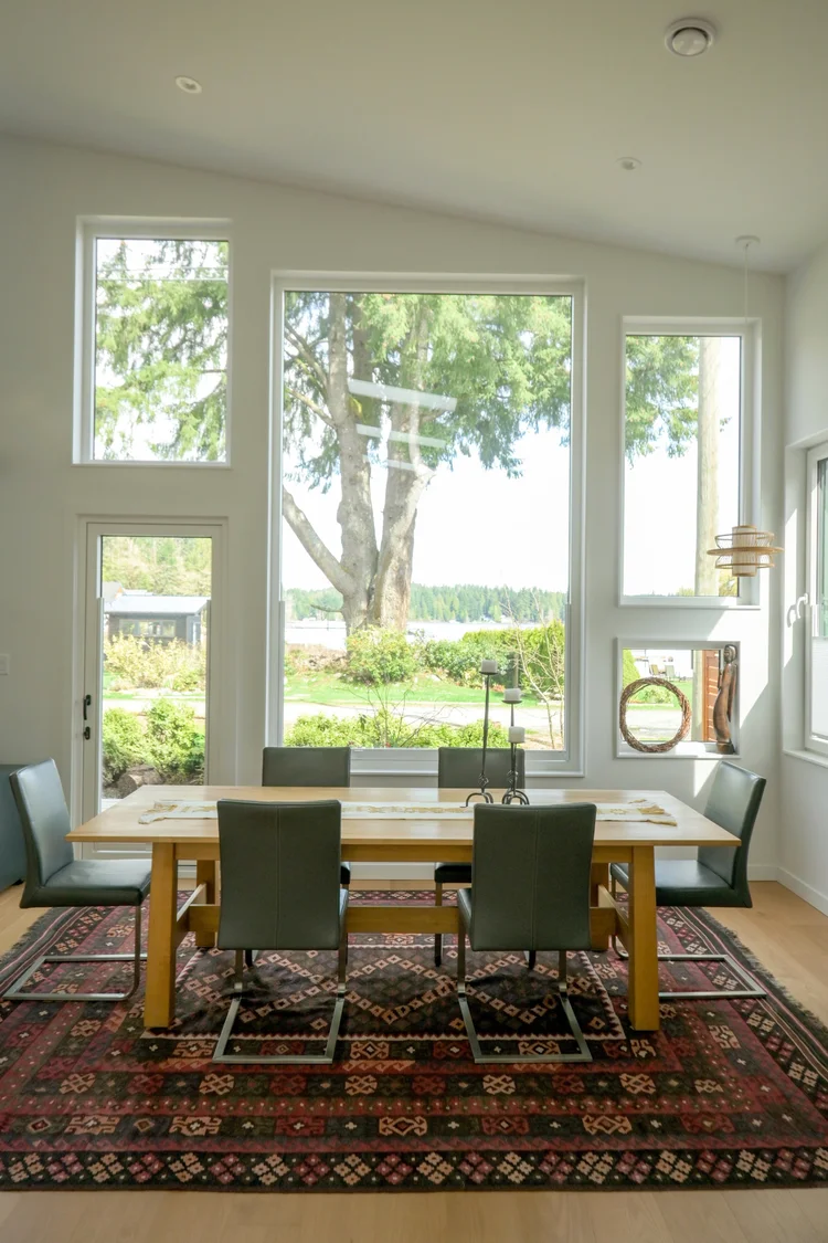 Modern two-story home with large glass windows, warmly lit interiors, and a balcony. Surrounded by trees and a manicured lawn at dusk. Cozy ambiance.