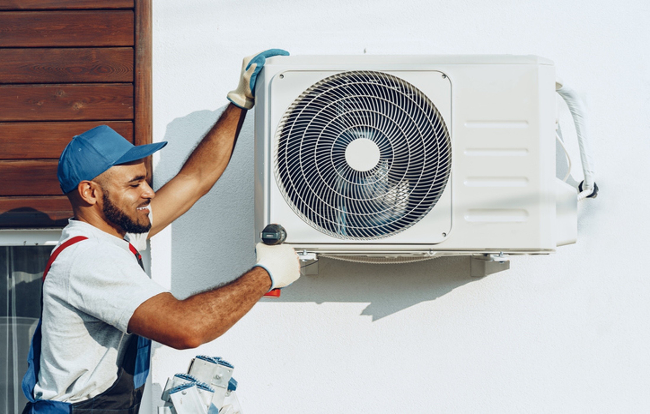 Home HVAC technician mounting an outdoor heat pump system on a wall bracket