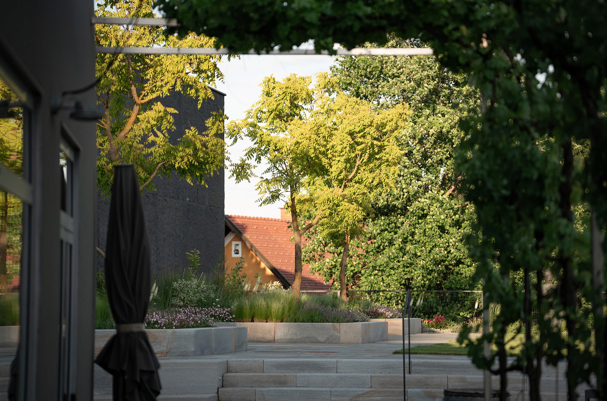 Moderner Garten mit Naturstein-Treppen, bepflanzten Hochbeeten und schattenspendenden Bäumen.