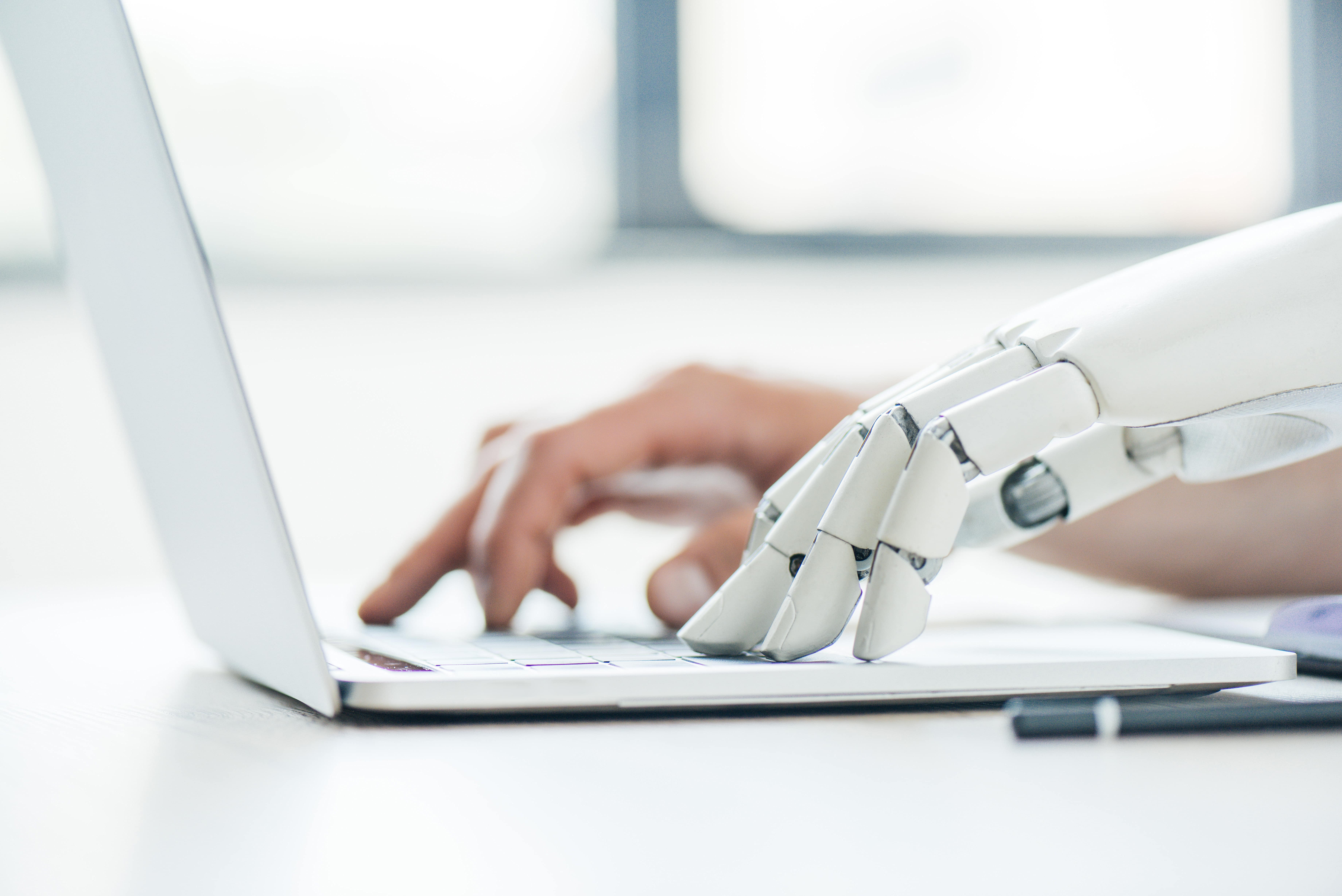 A high-tech robotic prosthetic hand types on a laptop, illustrating the future of work with AI, bionics, and human-computer collaboration.