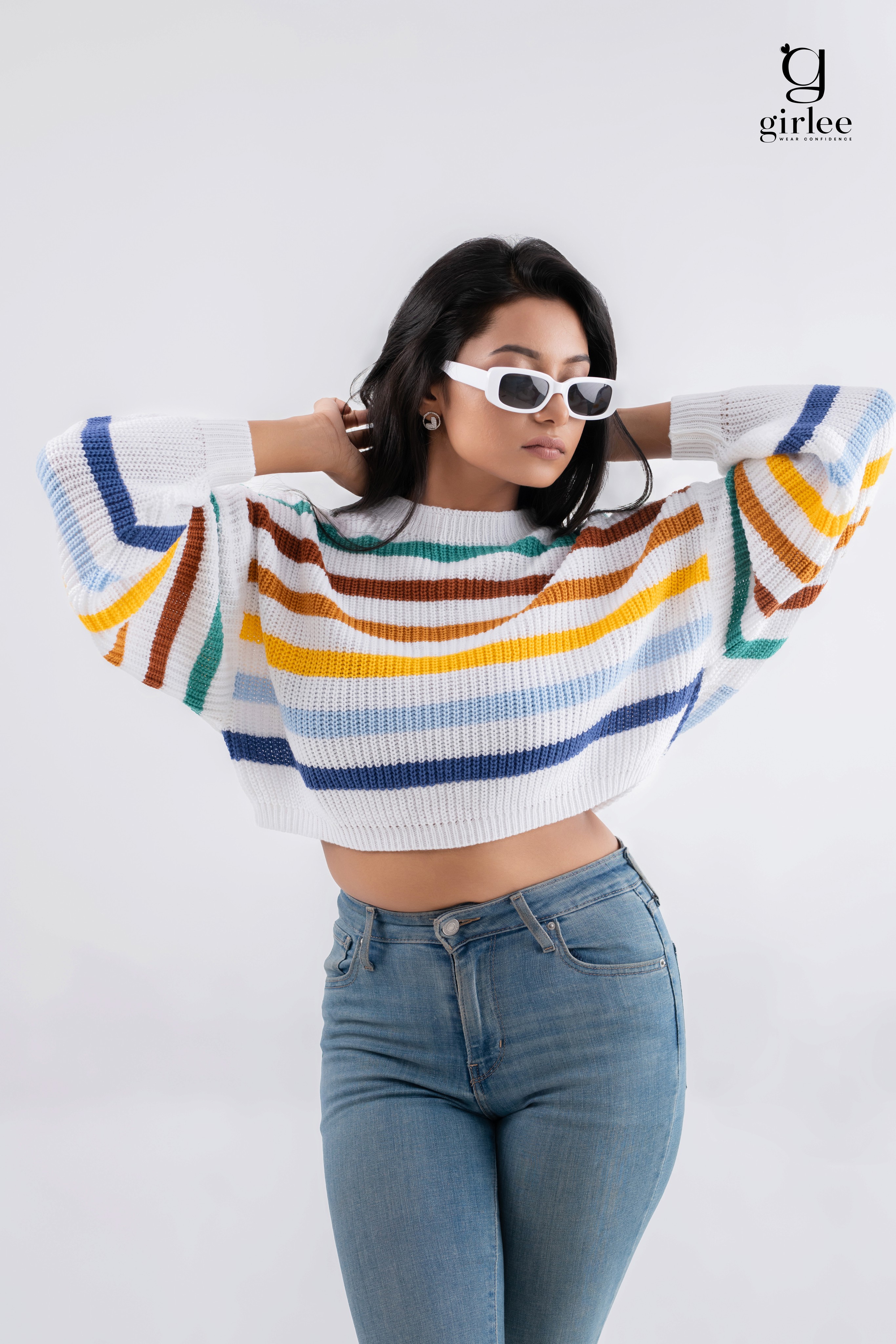 A smiling woman with her arms crossed, standing against a dark green background. She has long, dark hair.