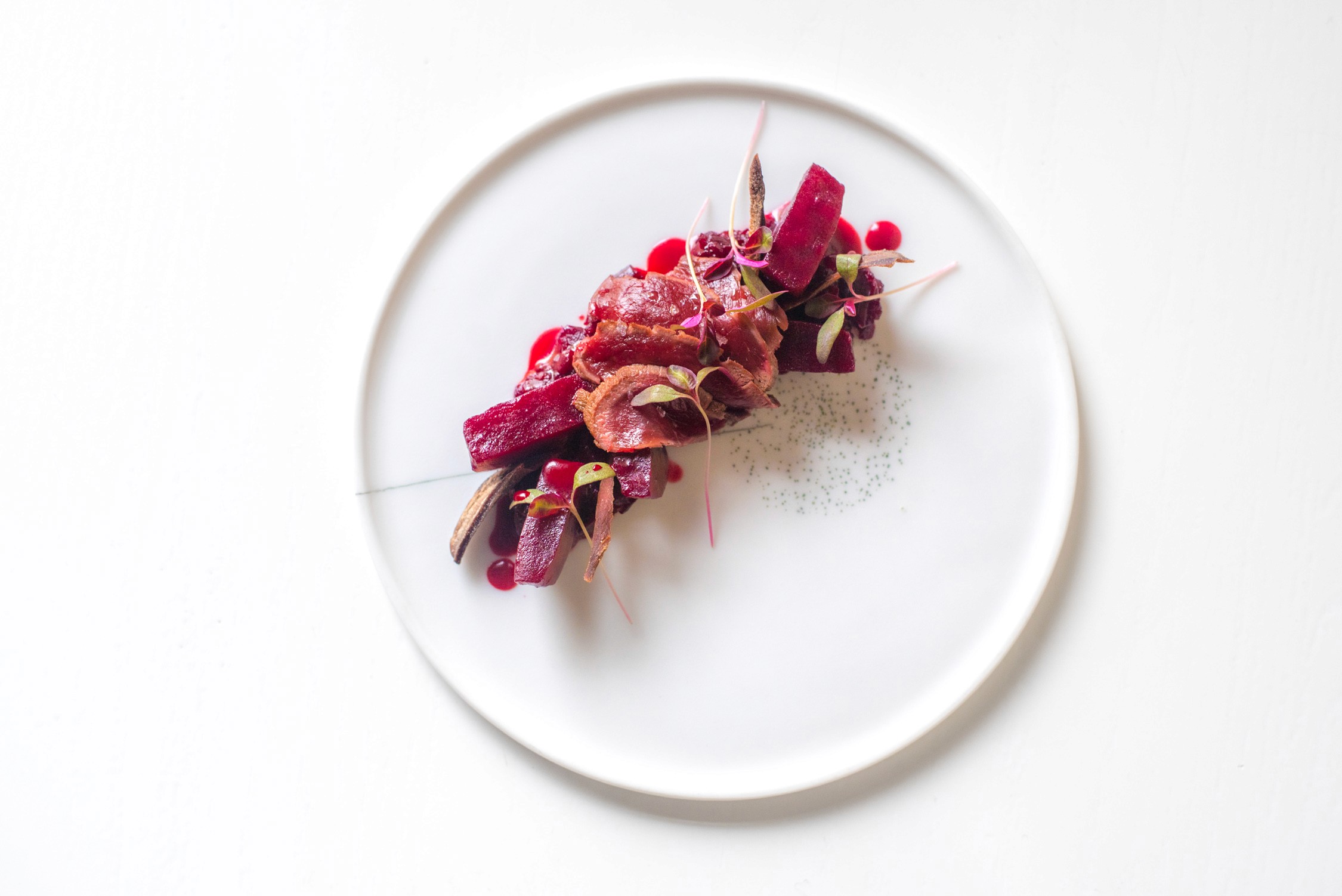A gourmet dish featuring seared tuna and red beet petals garnished with microgreens on a white plate against a white