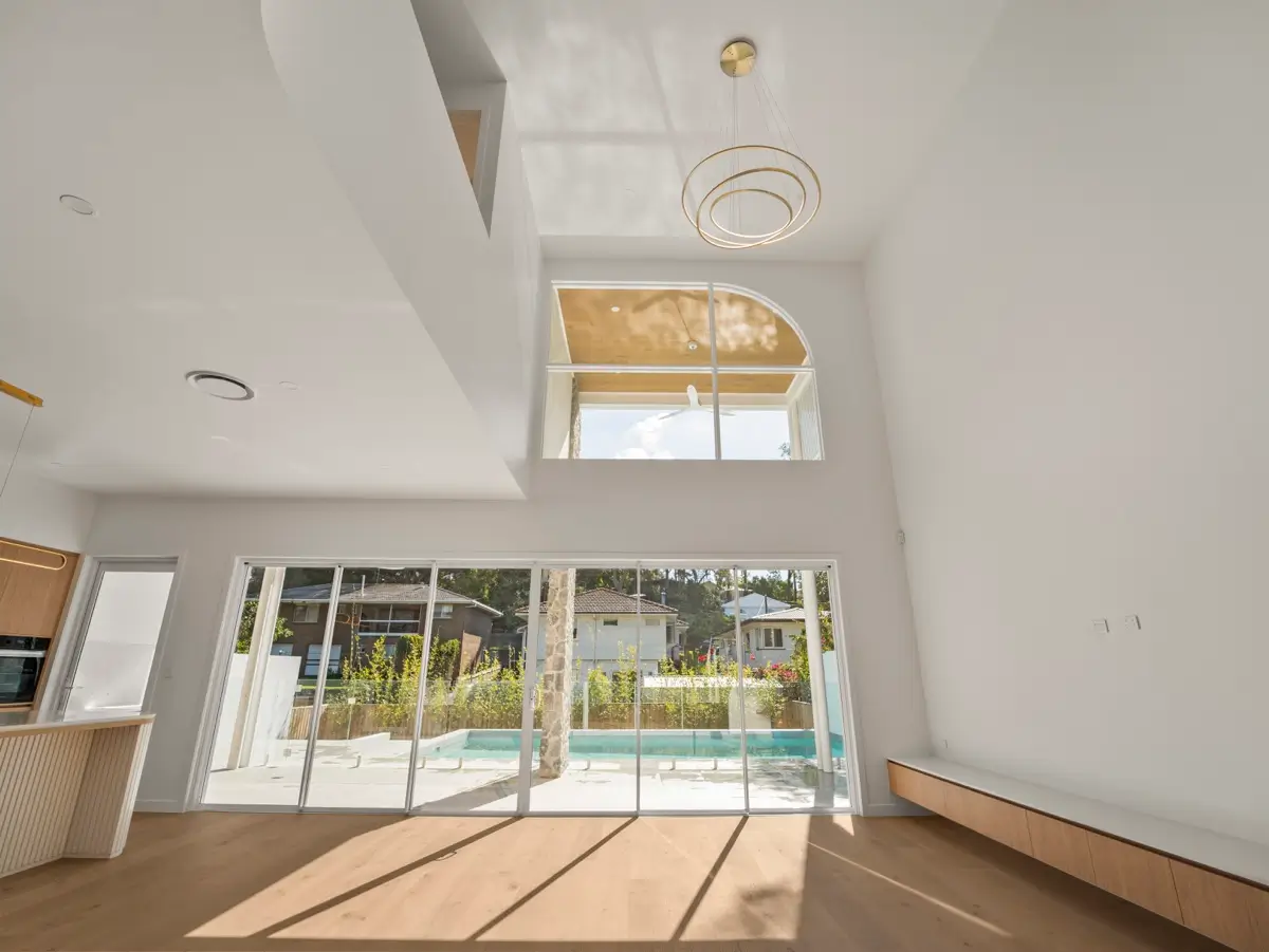 Double-height living space in a Brisbane home with a light-filled void and arched upper window, opening onto the outdoor pool via sliding glass doors
