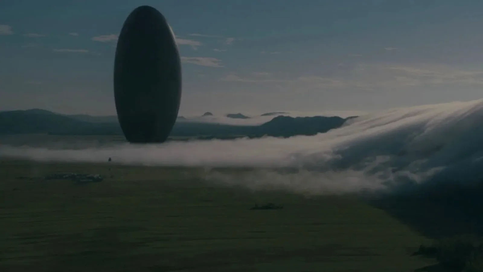 A mysterious, large, oval object stands vertically amidst a foggy landscape, surrounded by low clouds rolling over green fields, creating a dramatic and enigmatic scene that evokes a sense of wonder and curiosity.