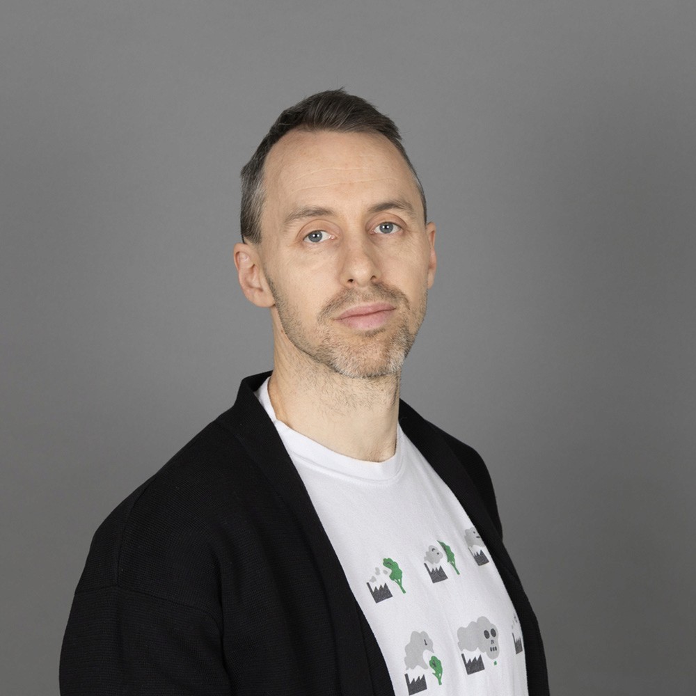 Portrait of Sandro Tagliavini founder and sole owner of Blite.ch. Portrait was taken in a studio with a dark grey background and Sandro wears a black jacket and a white t-shirt and looks into the camera.