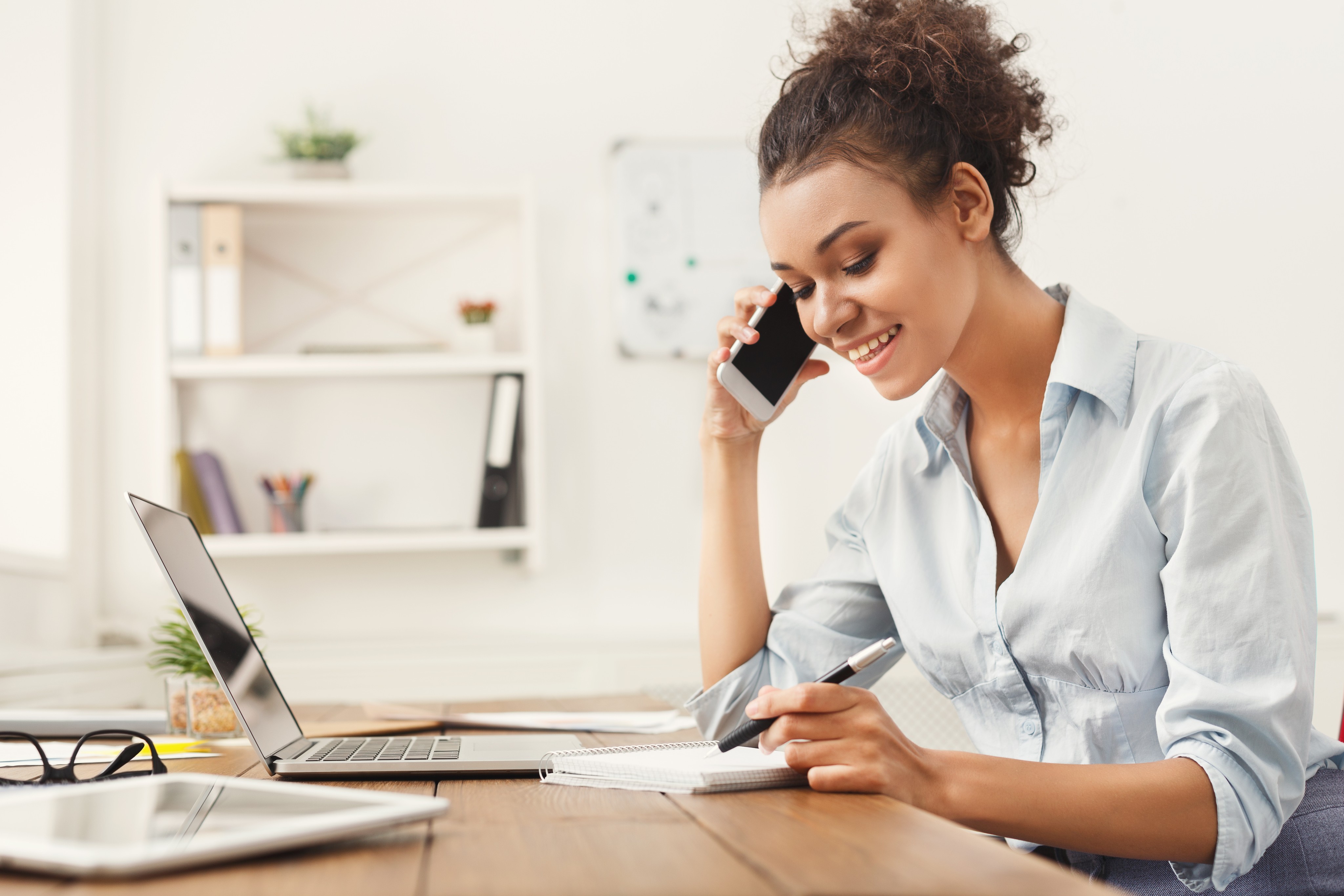 A woman speaking on the phone and writing in a notepad 