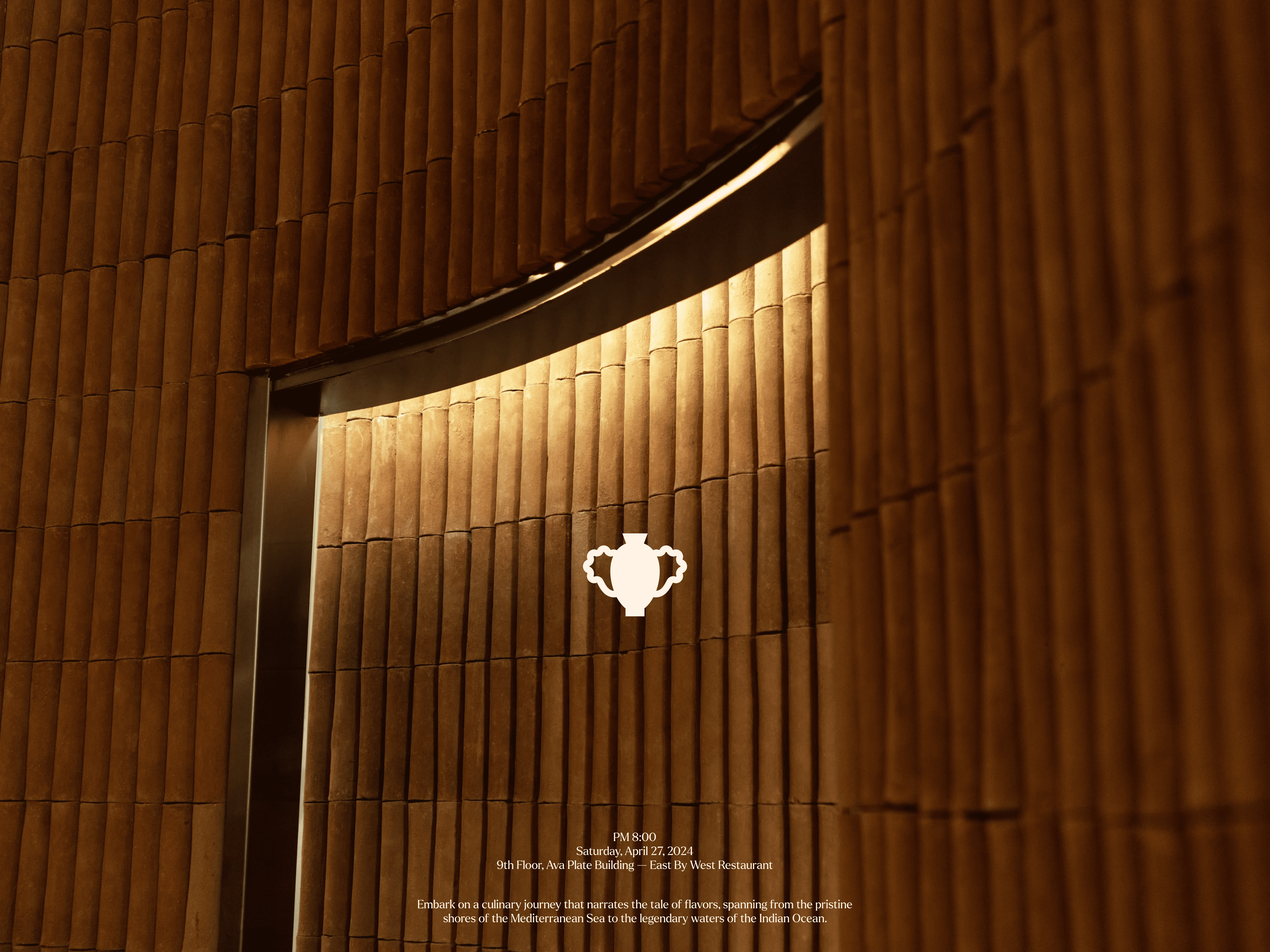 East by West restaurant entrance with illuminated wooden slat wall panels and ornate vase logo centered above the door. 