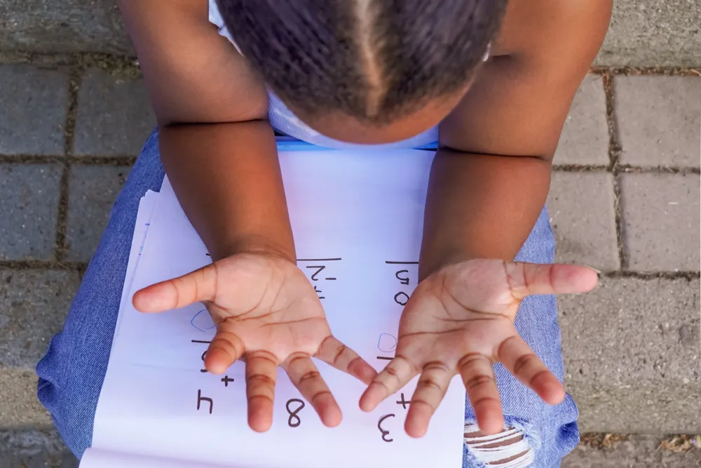 Child counting on their fingers with page of sums on her lap