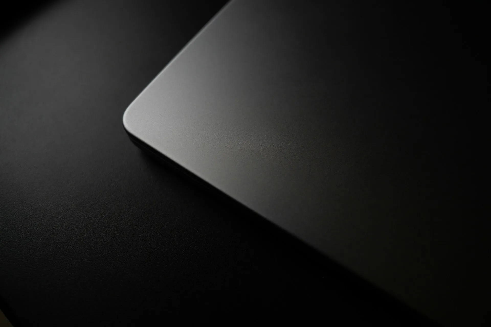 Matte dark gray laptop corner on a textured black surface.