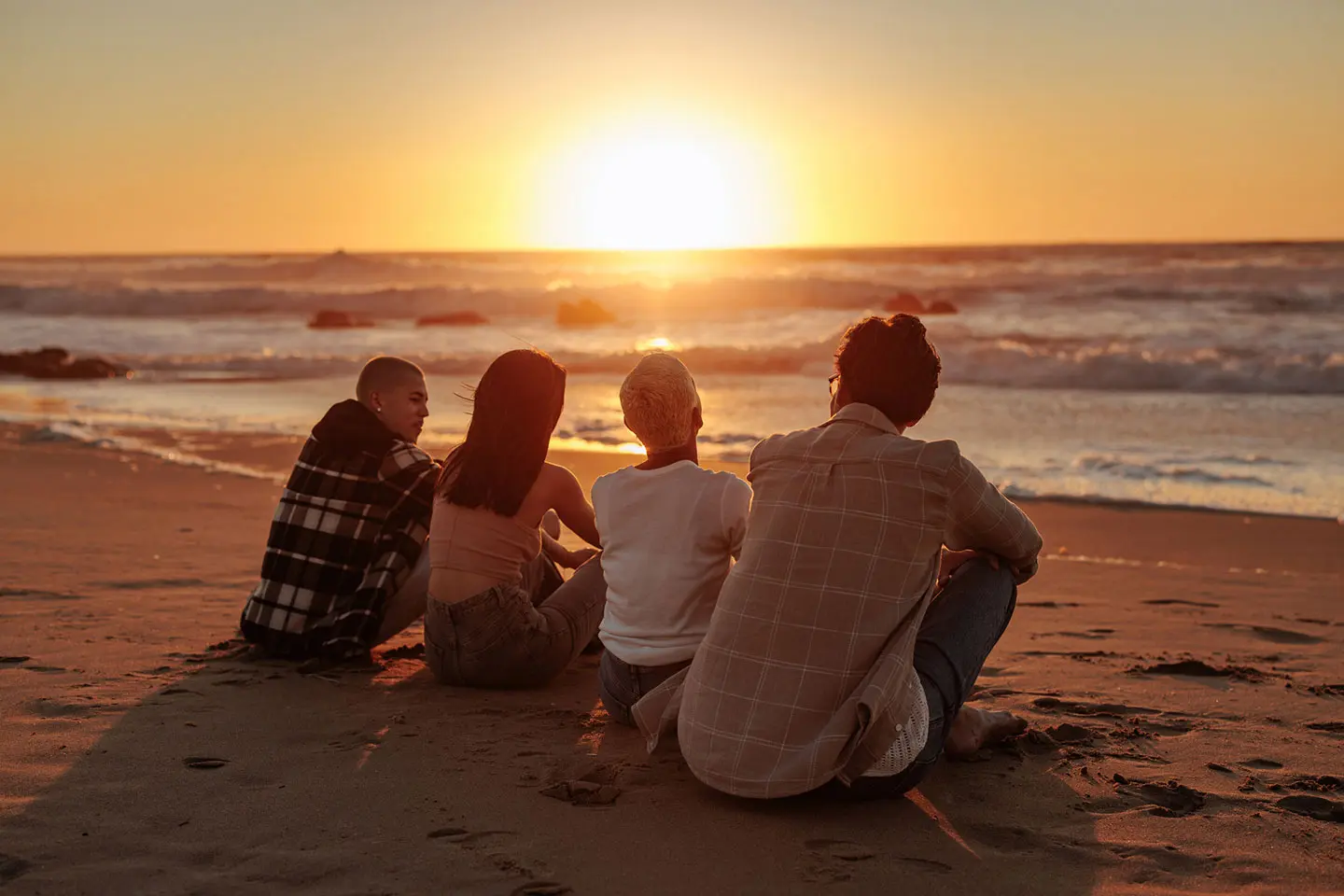 Four friends sitting on a beach at sunset watching the ocean, illustrating life satisfaction and meaningful personal connections outside of work