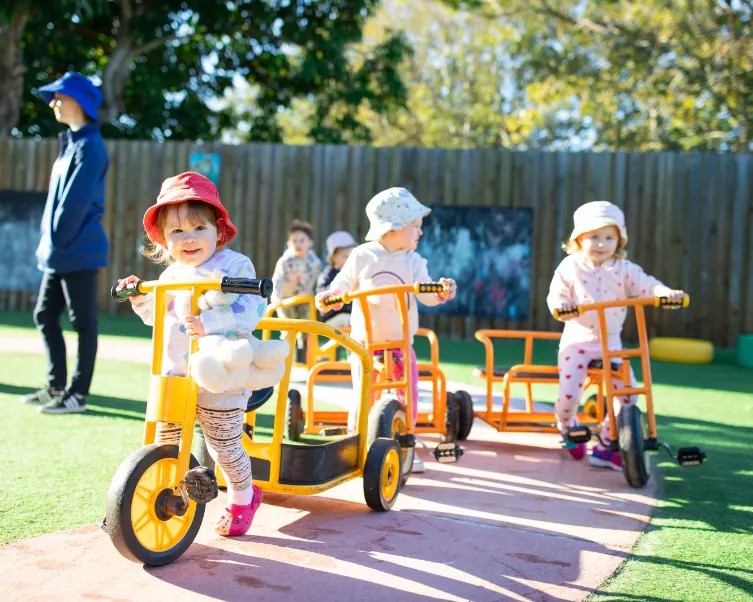 Children riding tricycles and playing outdoors on the bike track at Kaleidoscope Kids Booval childcare centre.