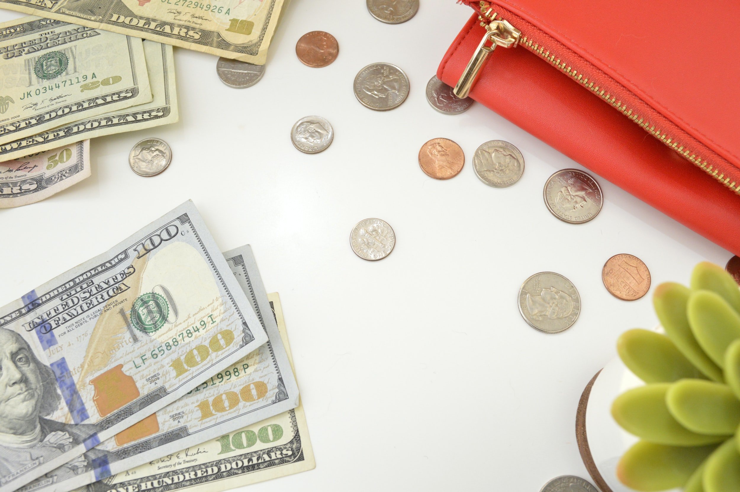 Banknotes, coins, a red purse and a small plant on a white surface