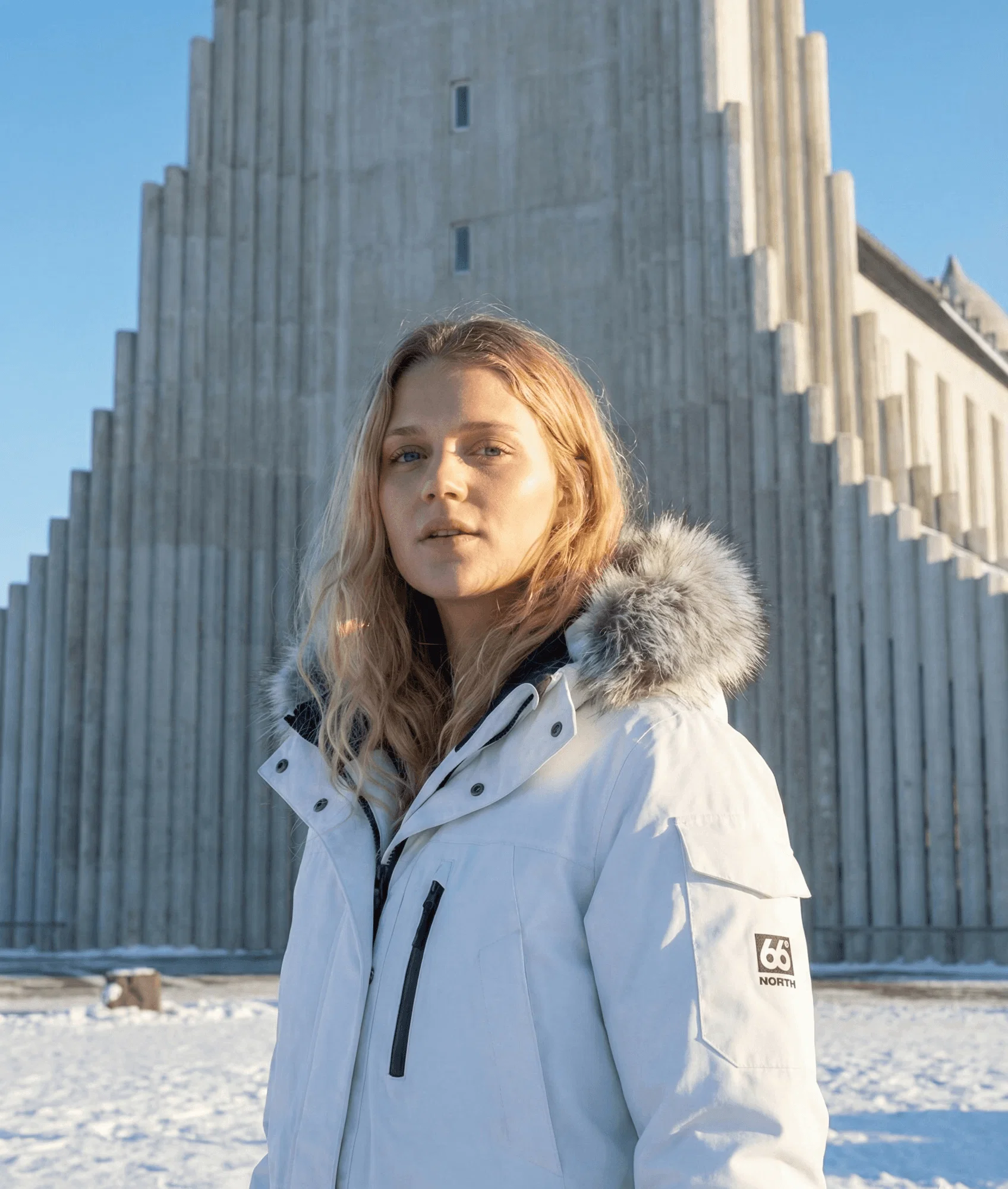 Woman in a white jacket standing in front of a concrete church.