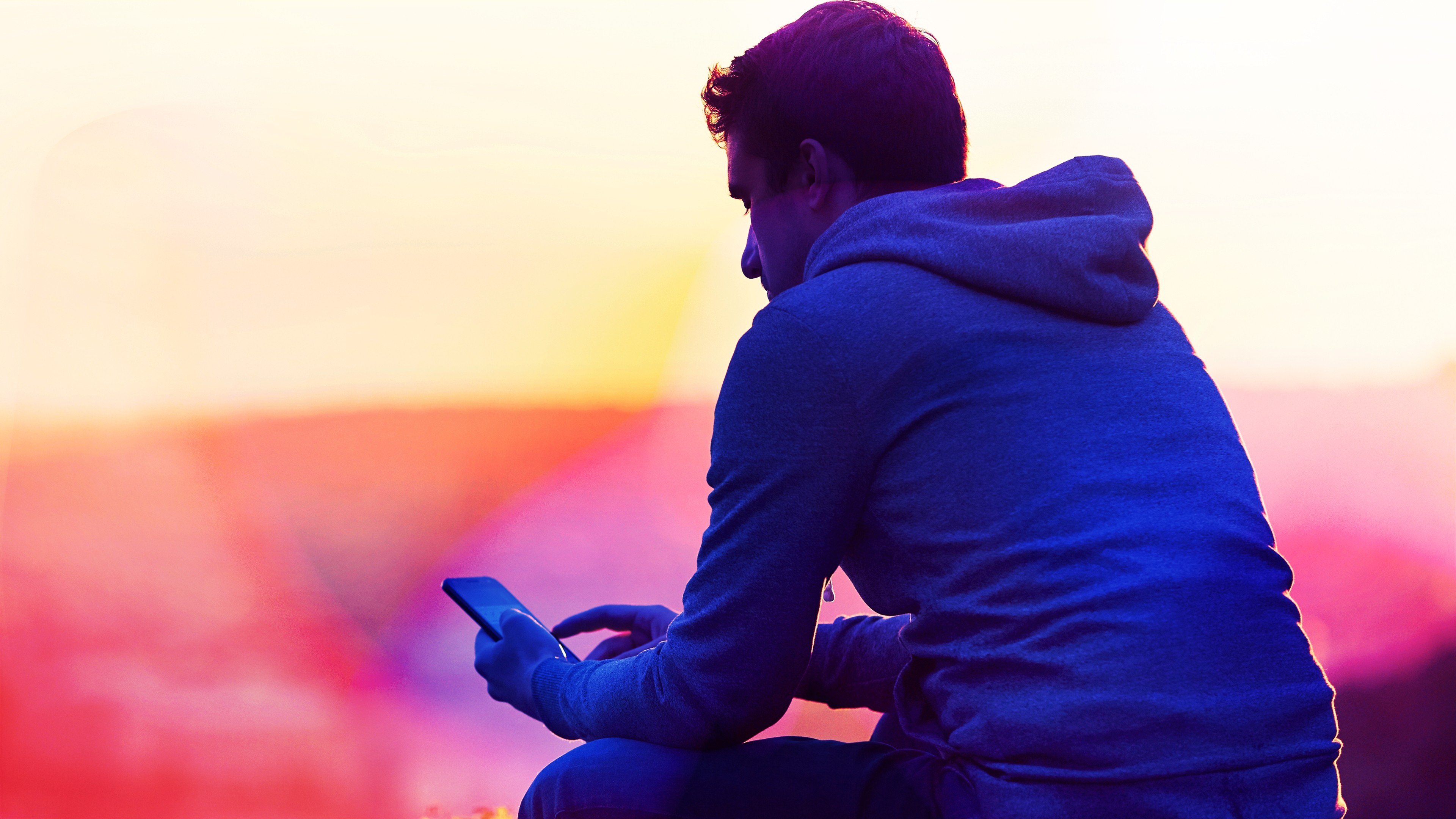 A man sits outside, at sunset, looking at his phone