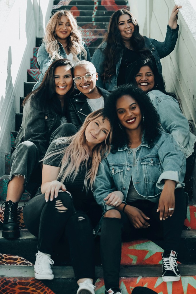 a group of seven young female friends sit together on an outdoor staircase. 