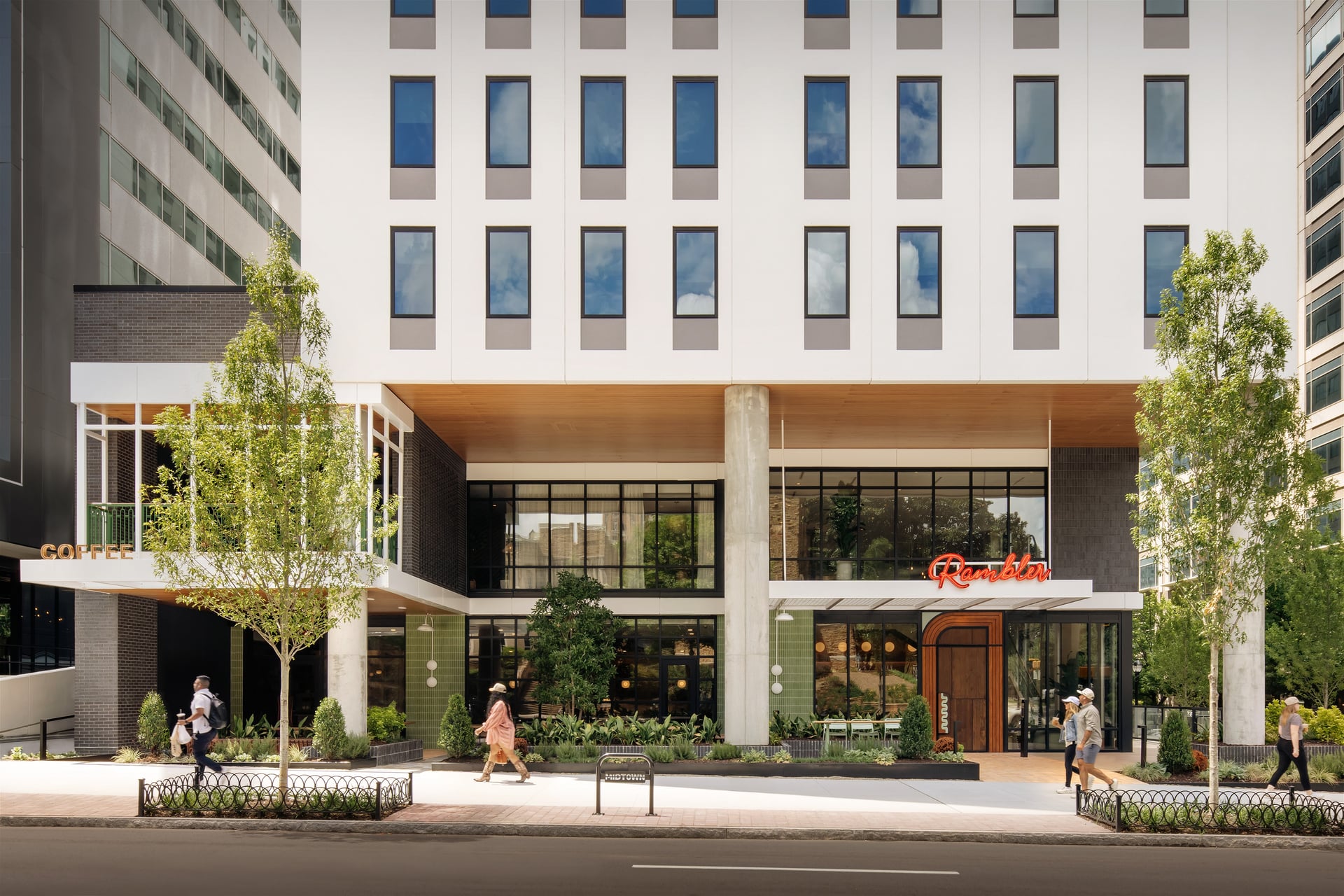 Exterior view of Rambler apartment building featuring street-level retail, modern white architecture, wood soffits, and glass storefronts.