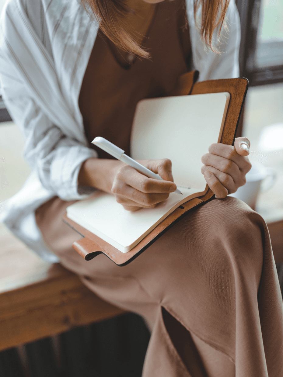 A woman is journaling while sitting in a taupe coloured dress