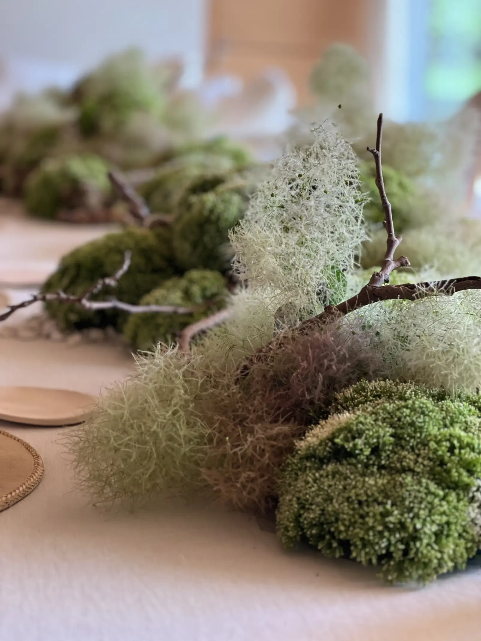 Centro de mesa con musgos verdes, ramas secas y piedras blancas, acompañado de vajilla minimalista y copas de cristal