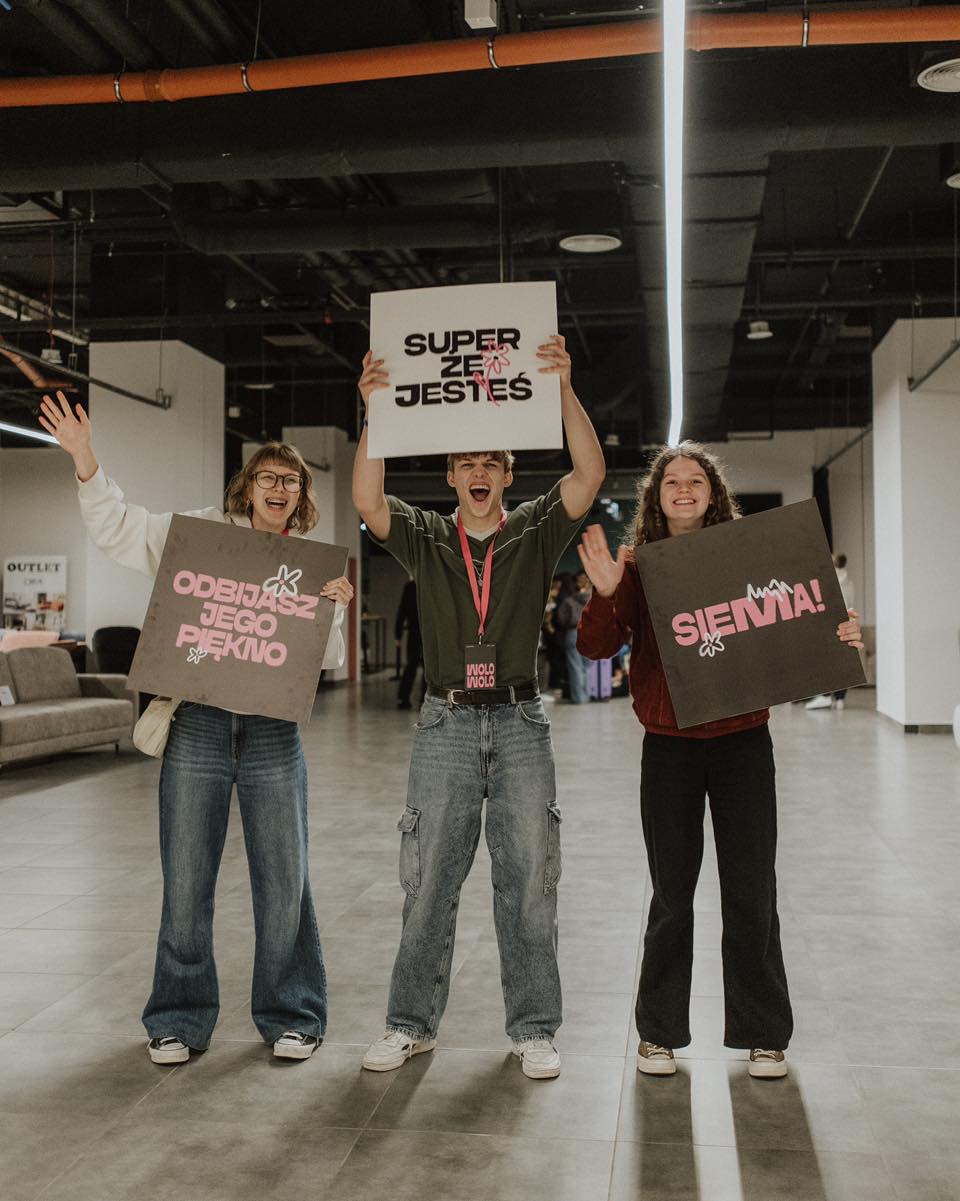 Uśmiechnięte trzy osoby trzymające plansze z hasłami powitalnymi