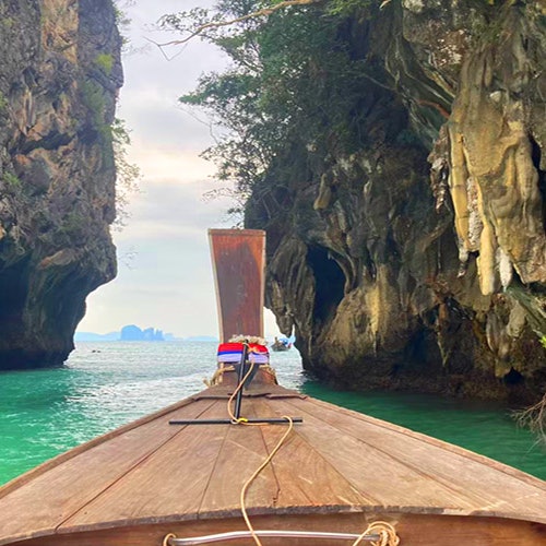 一艘木船在清澈的碧绿色水面上穿梭于两座高耸的岩石悬崖之间,背景是远处可见的岛屿。