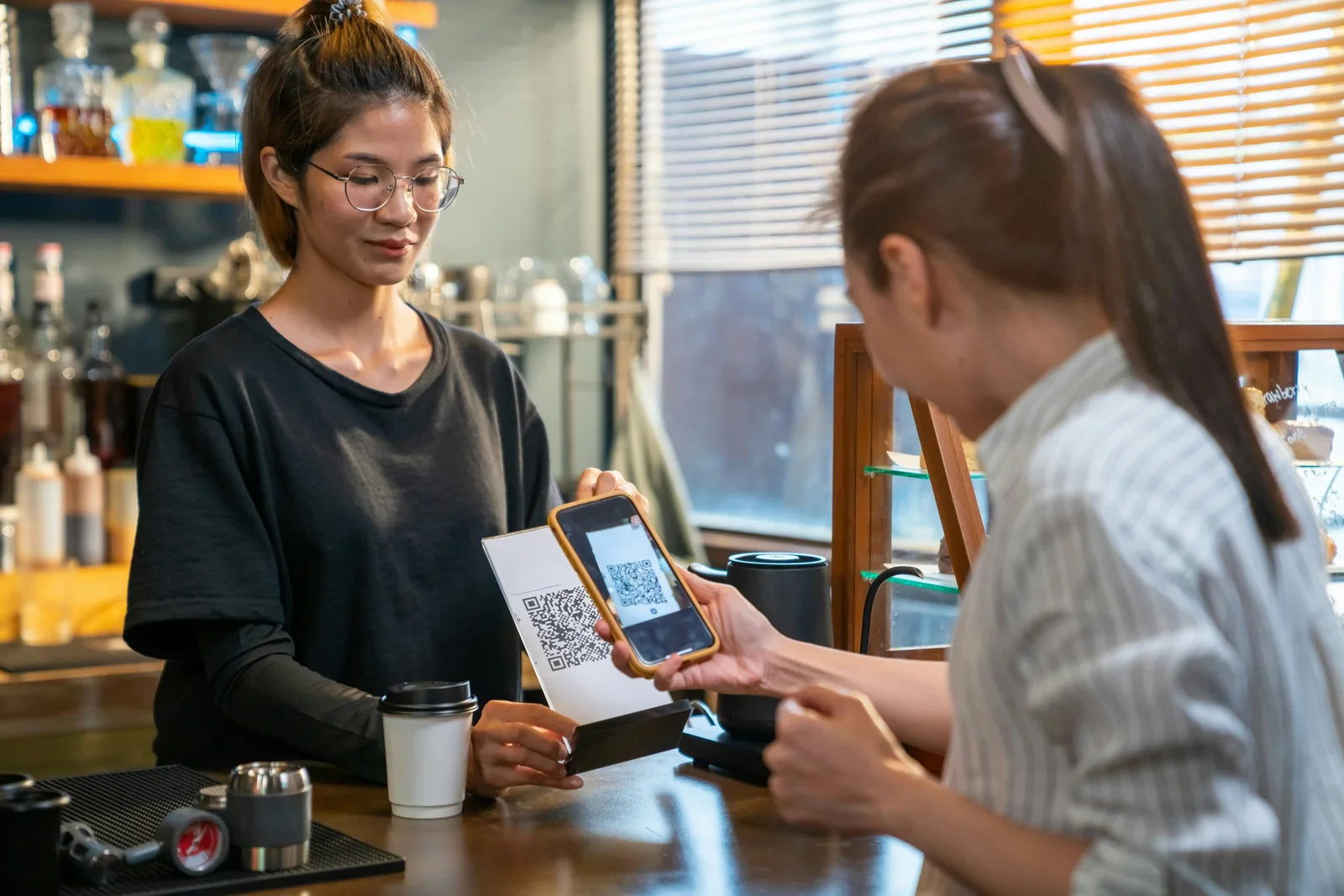 Customer scanning QR code on payment terminal at coffee shop counter during transaction.
