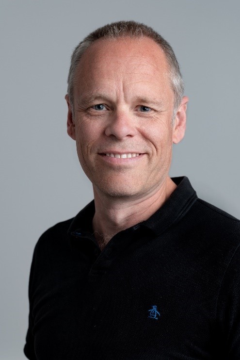 Smiling young man in a black t-shirt against a gray background, radiating warmth and friendliness.
