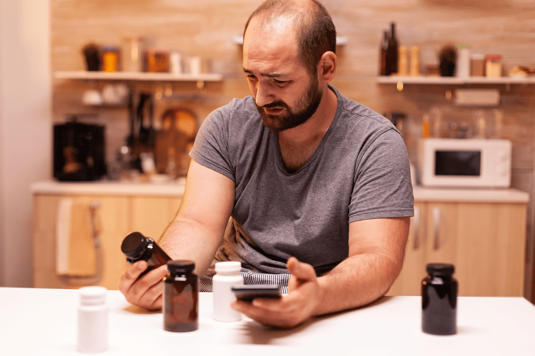 Man sitting at a kitchen counter looking at pill bottles, representing health issues linked to mold exposure