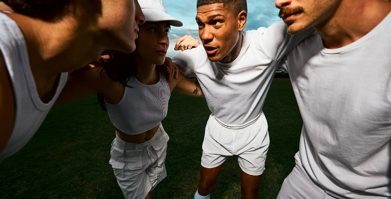 Friends in white sportswear huddling together on a grass pitch