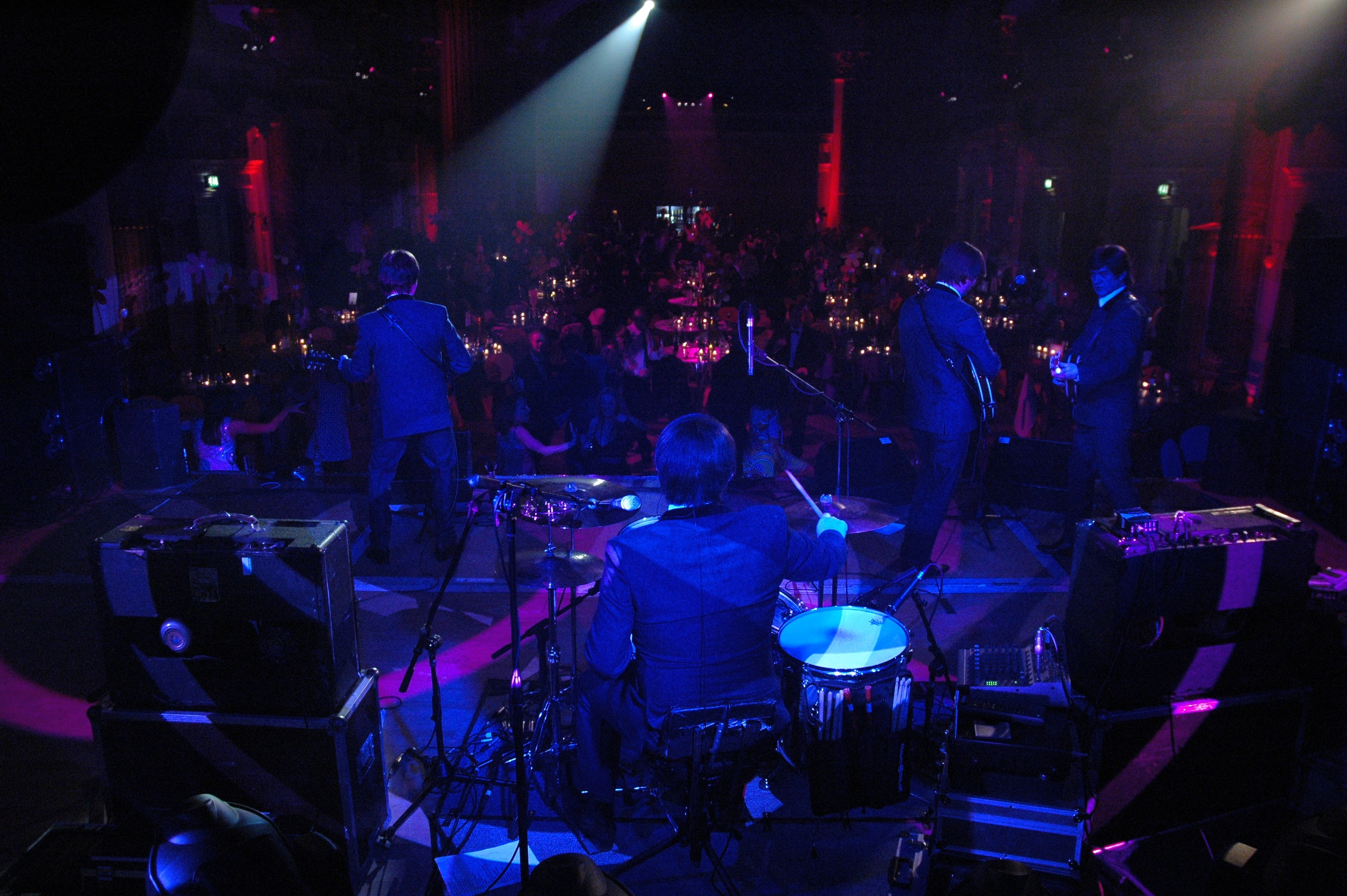 Live band performing on stage at a corporate party, with guests gathered beneath colourful event lighting.