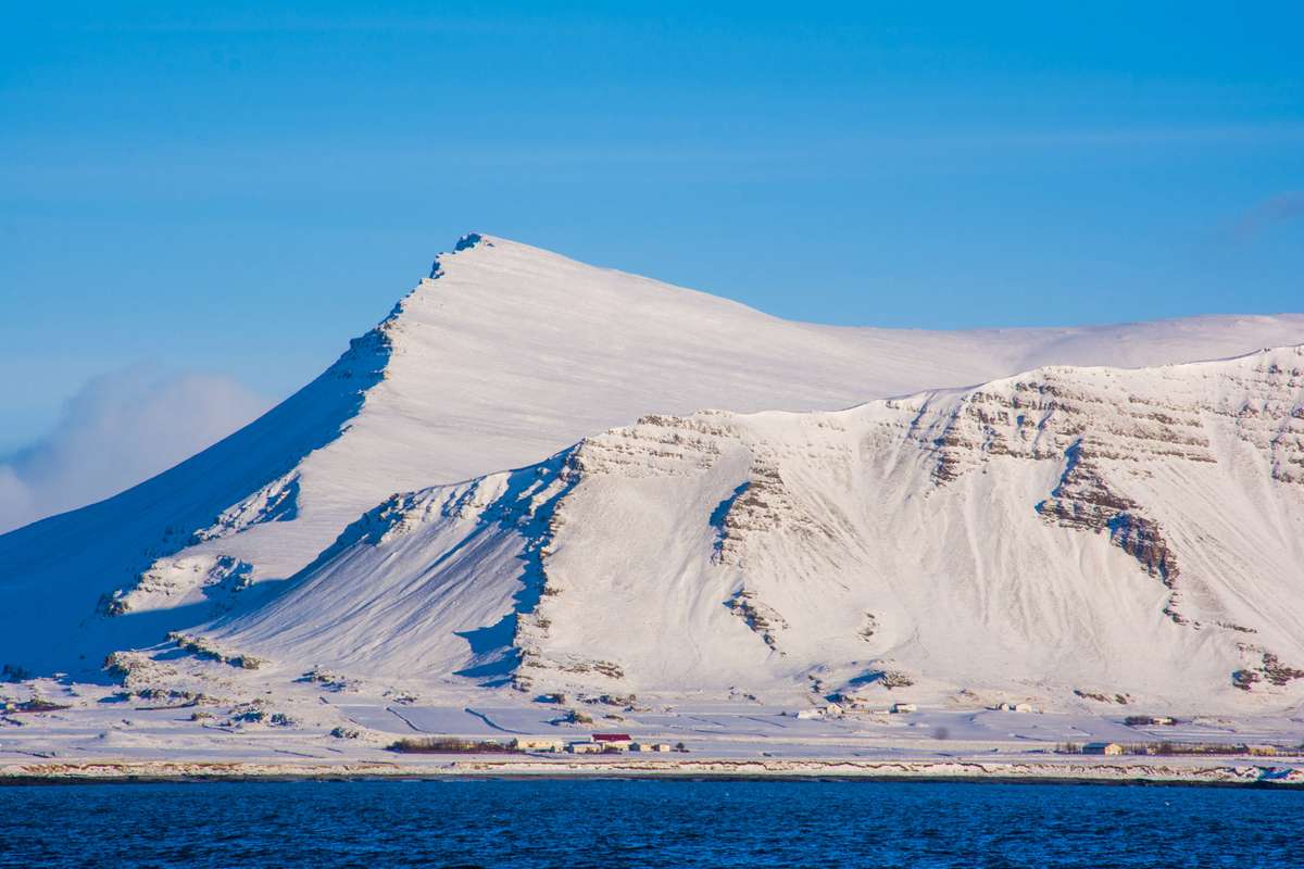 Snow-covered mountains and icy cliffs rise above a frozen body of water under a clear blue sky.
