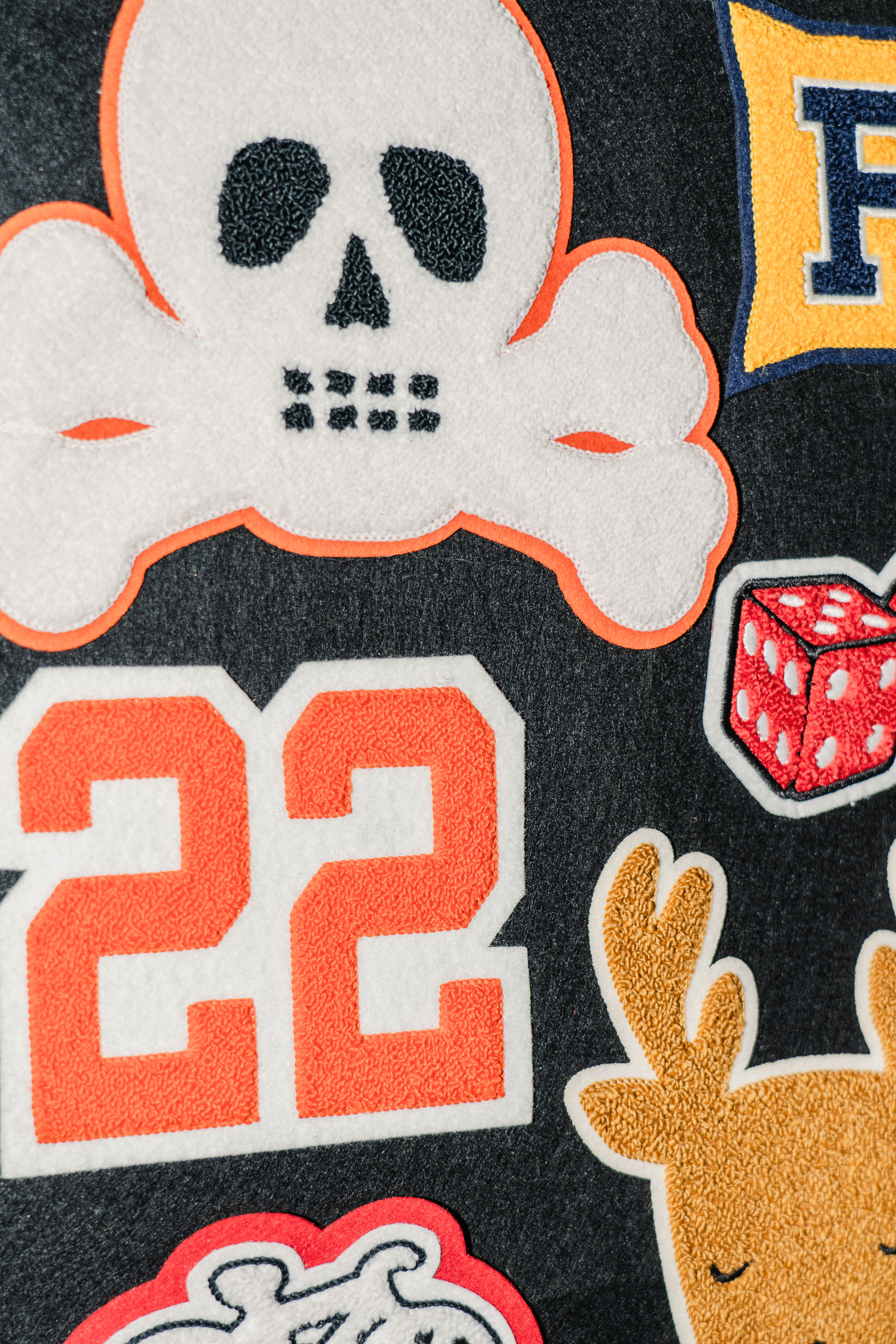 Assorted chenille patches on a black felt, there is a skull, a deer, some dice, an orange 22.