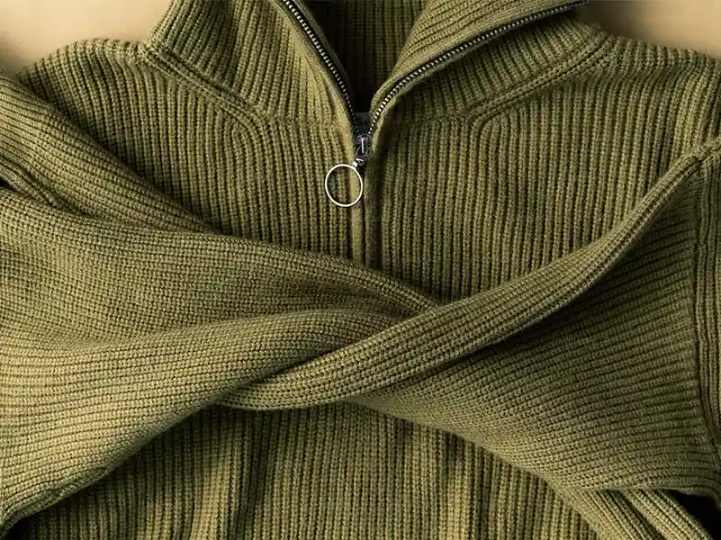 A highneck heavy knit sweater laid flat with the zipper open