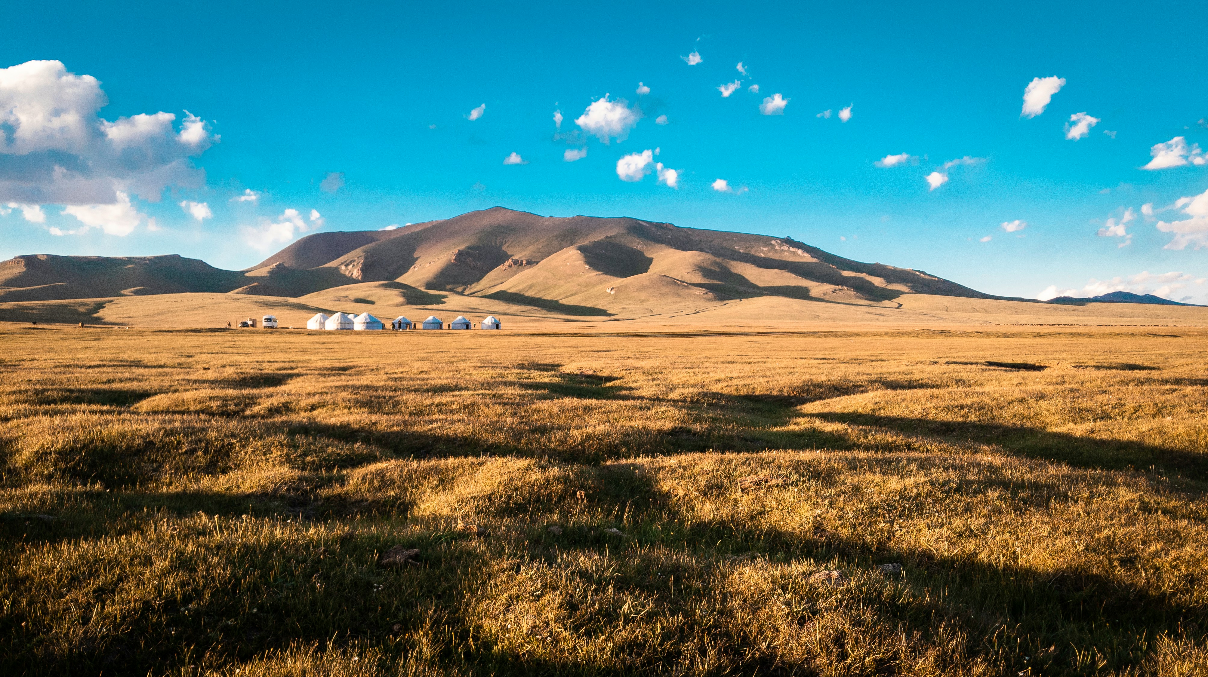 green grass field near mountain under blue sky during daytime