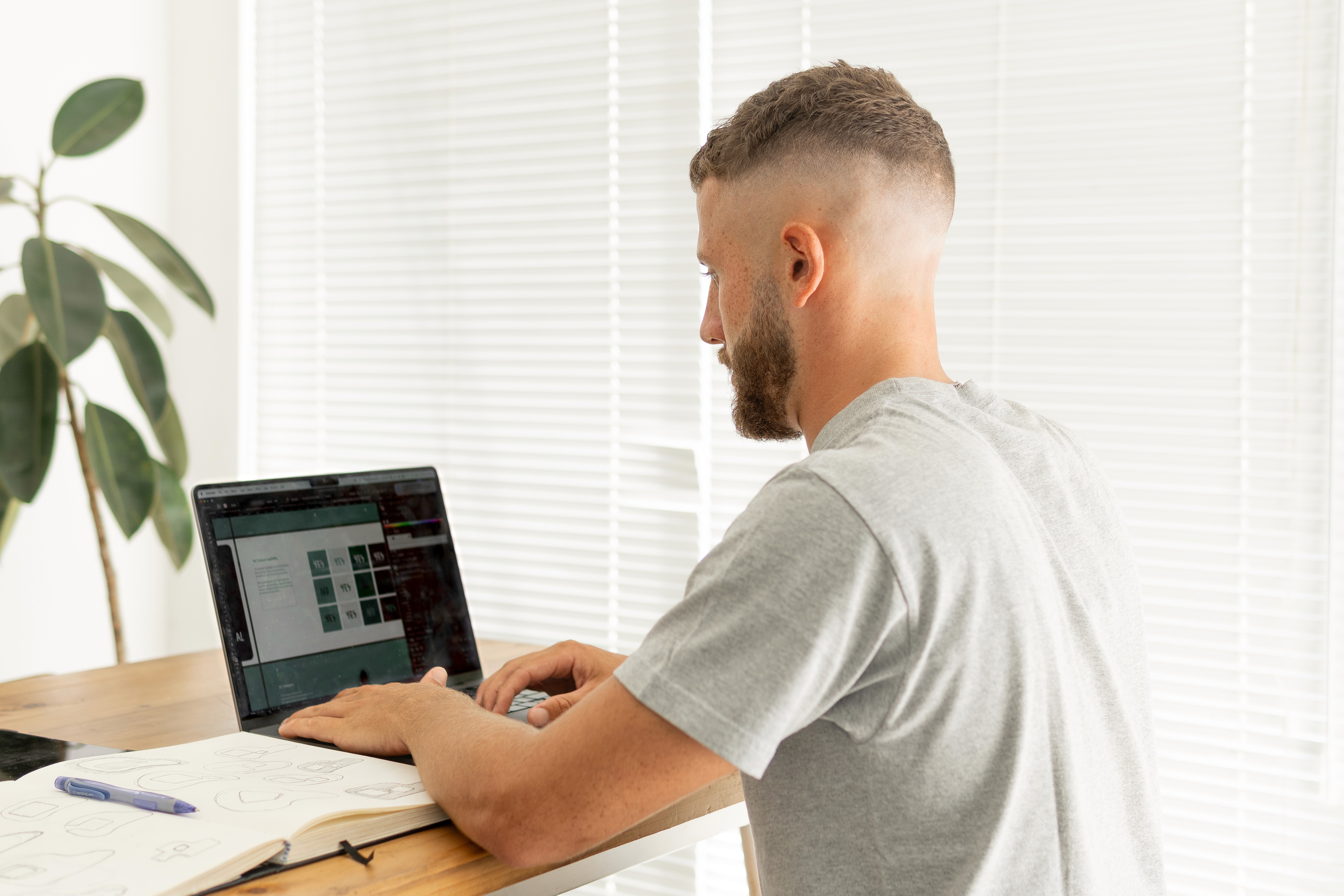 Person wearing black clothing carrying a black tote bag with a green globe-like geometric symbol, standing against a concrete wall in sunlight and shadow.