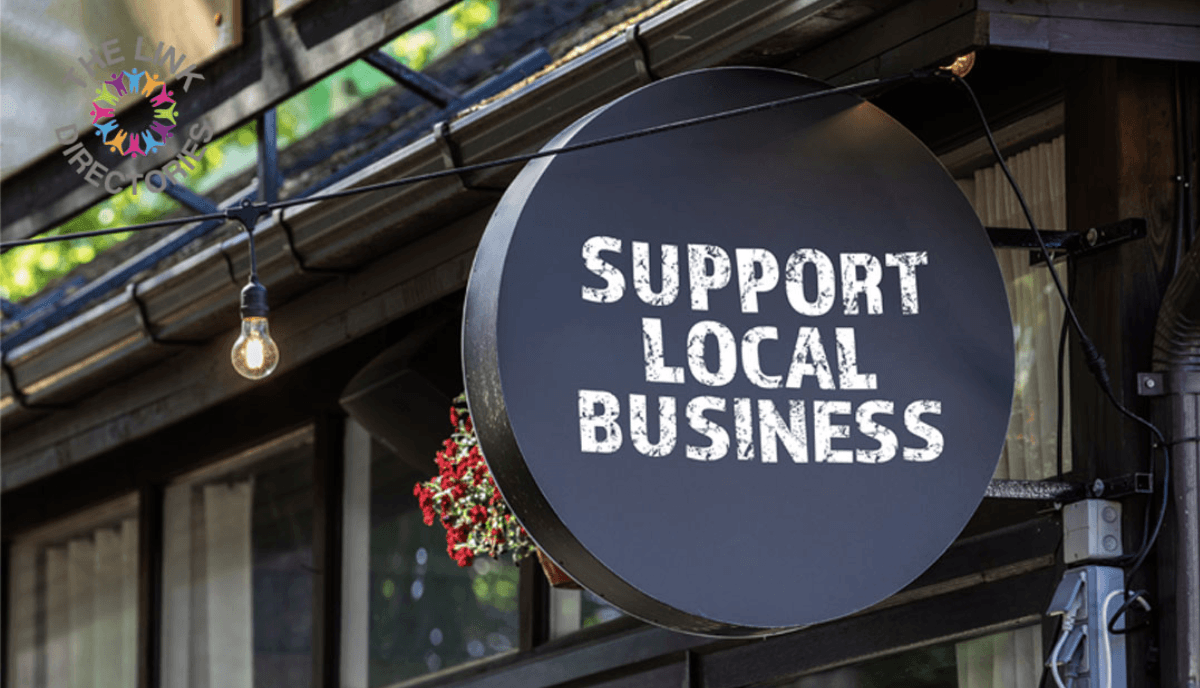 A smiling man with curly hair is sitting at a desk, looking at the camera, with a laptop and a lamp in the background.