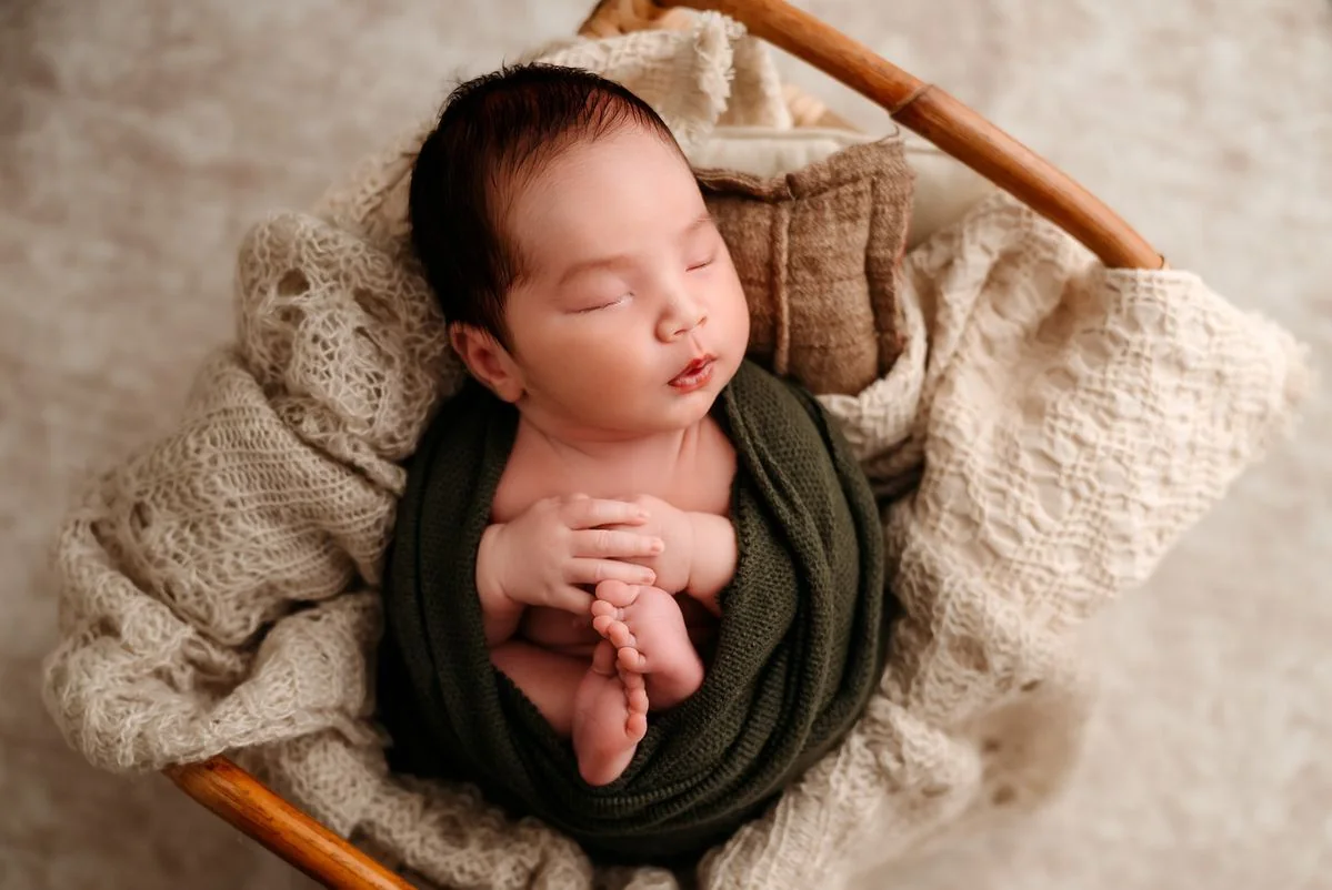 Sleeping newborn in a dark green wrap in a wooden basket