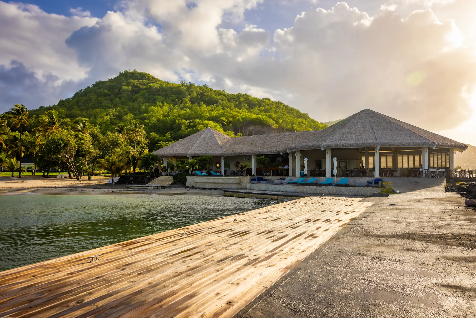 Beachfront villas framed by palm trees and lush green hills, overlooking calm turquoise water