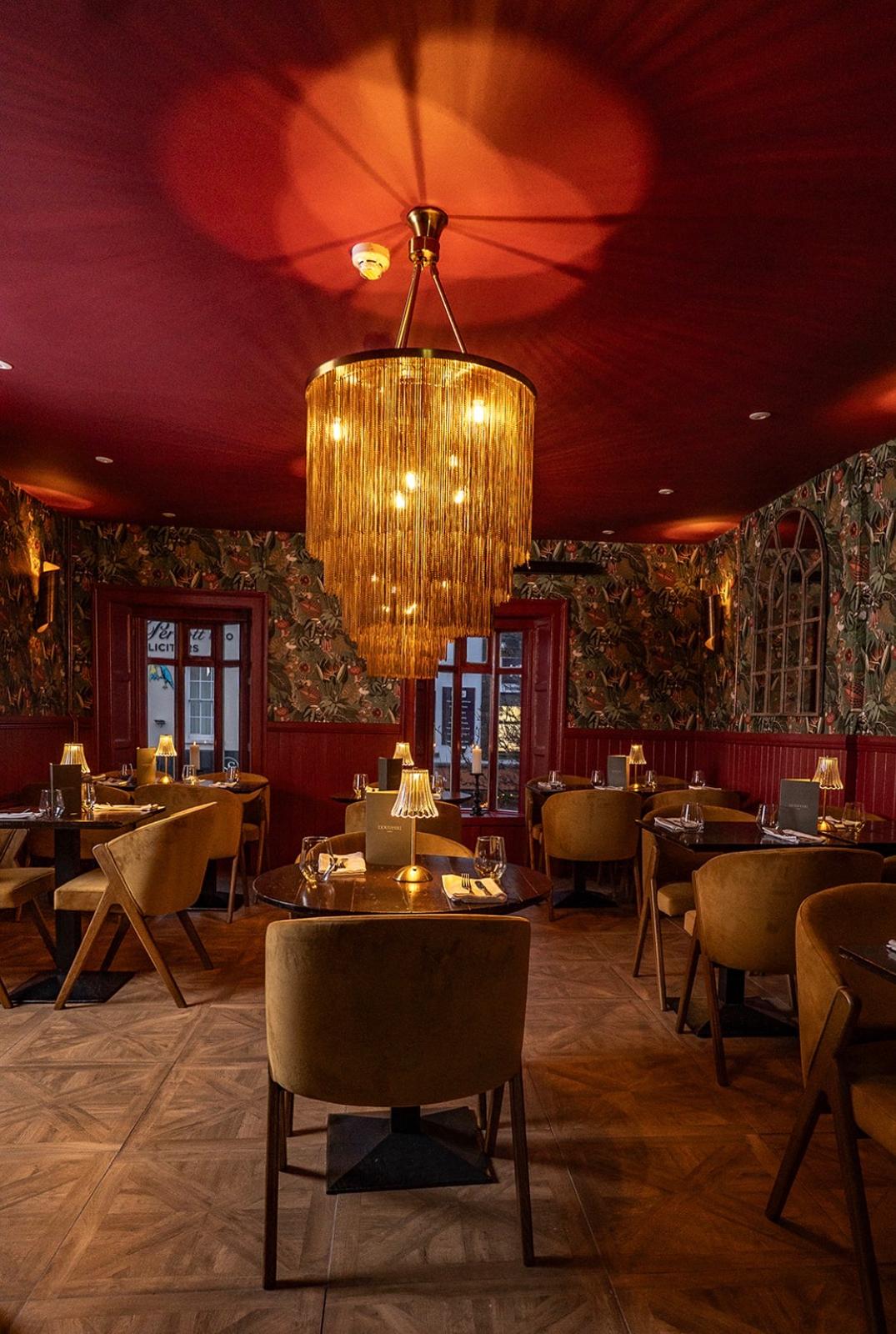 Cozy cafe corner with a round terrazzo table surrounded by wooden chairs, decorated with potted plants and a large mirror reflecting warm light.