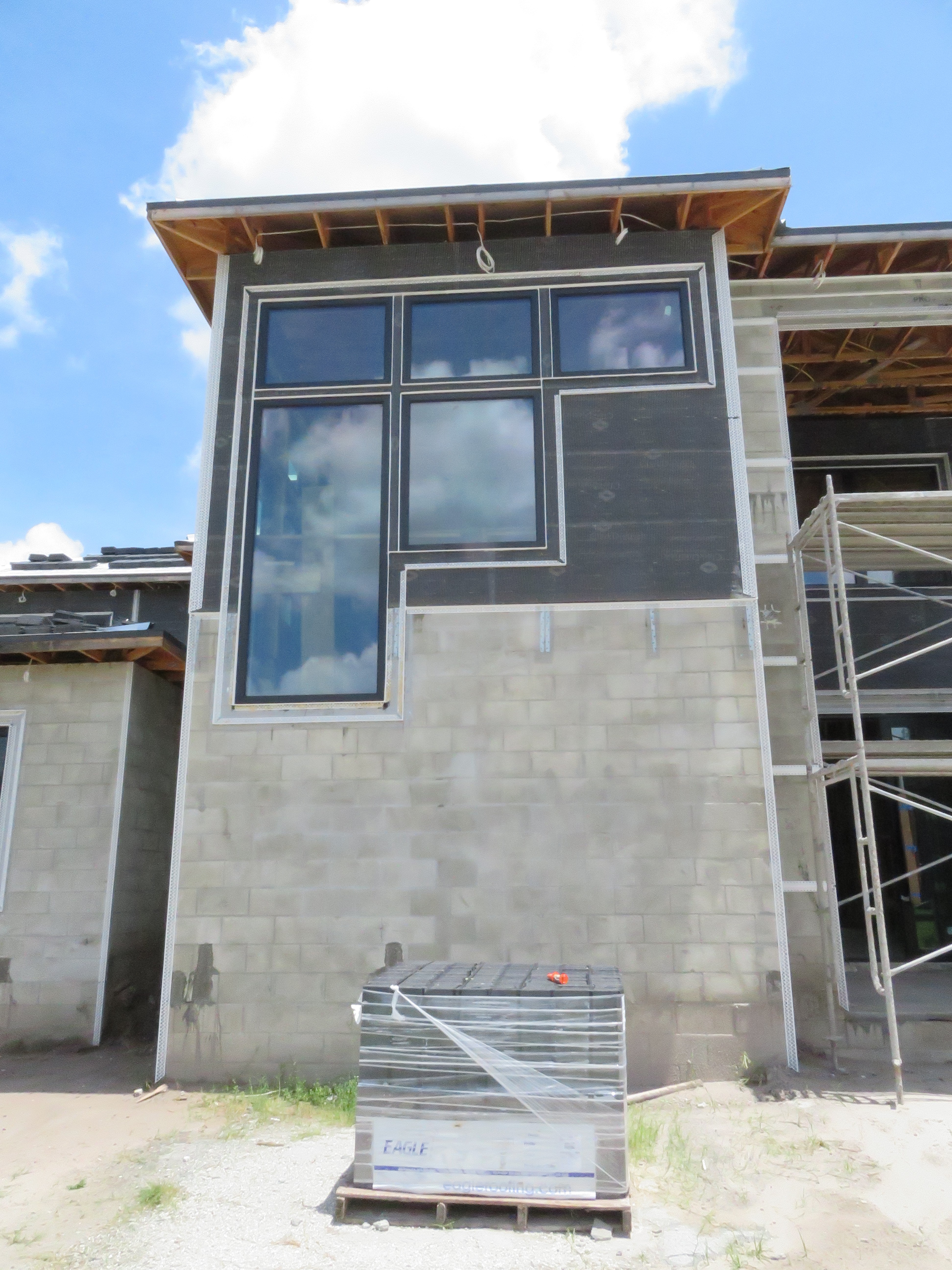 Modern house under construction with unique L-shaped window on cinder block wall.