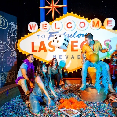 Five people in front of a "Welcome to Fabulous Las Vegas" sign, surrounded by colorful decorations and confetti.