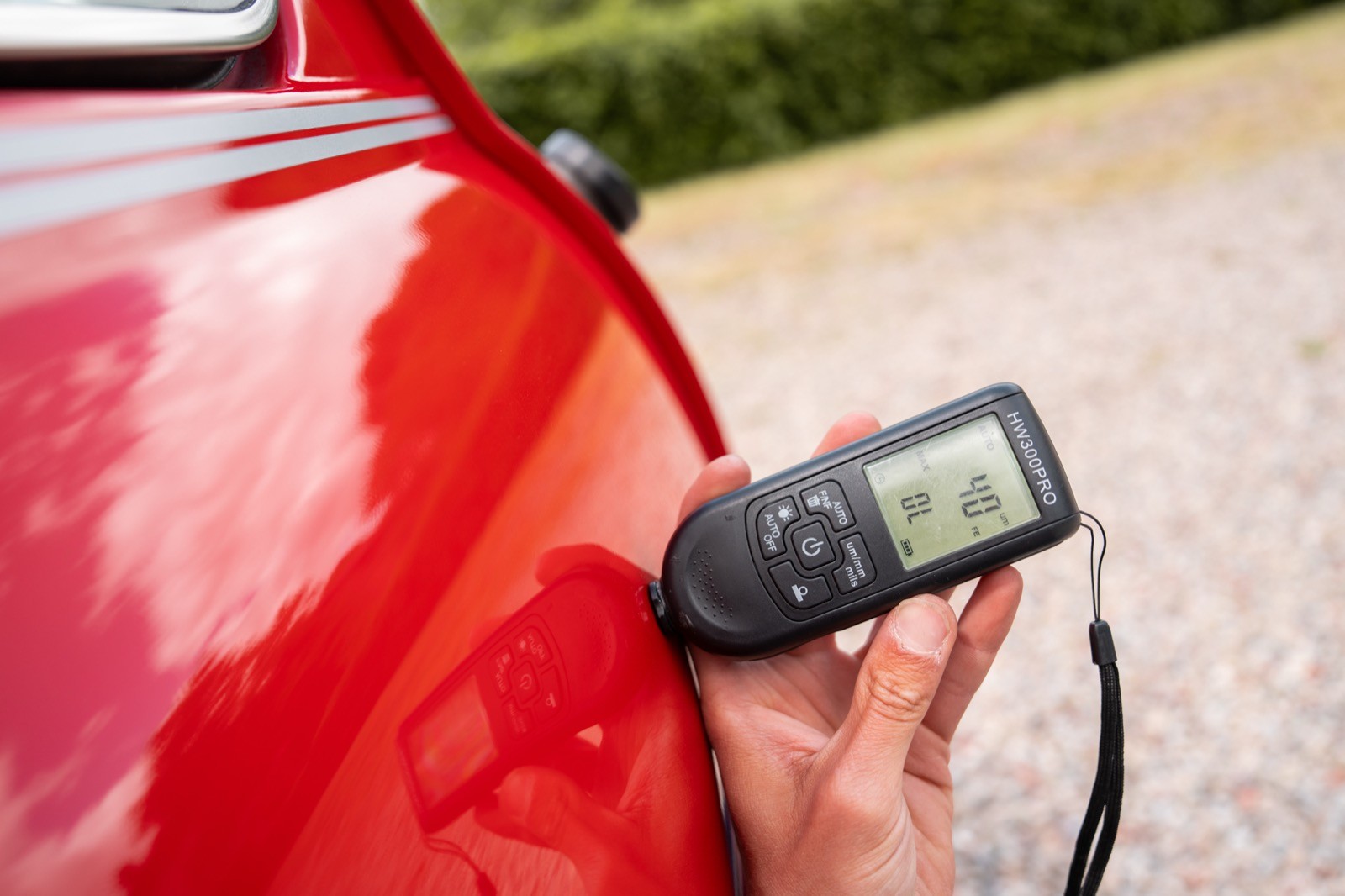 A person using a device to measure the paint thickness on a red car's exterior.