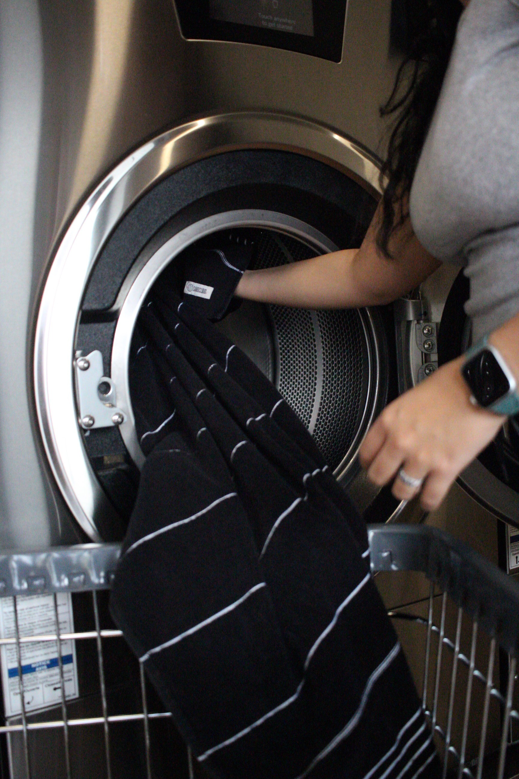 Person loading clothes into a commercial washing machine, showing everyday operations that buyers should observe when learning how to buy a laundromat.