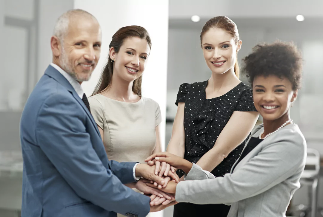 Four colleagues holding hands together as team effort