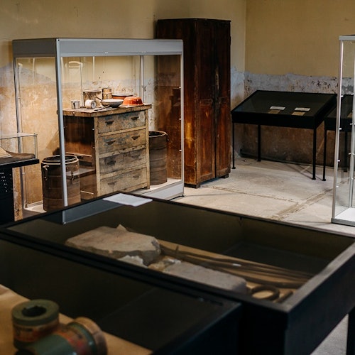 Museum exhibit room displaying vintage items, including tools, wooden barrels, and glass cases with artifacts on display.