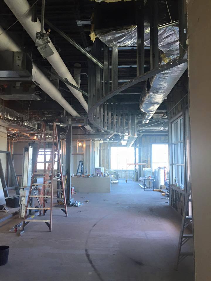 An unfinished interior space with exposed beams, scaffolding, and large windows letting in natural light.