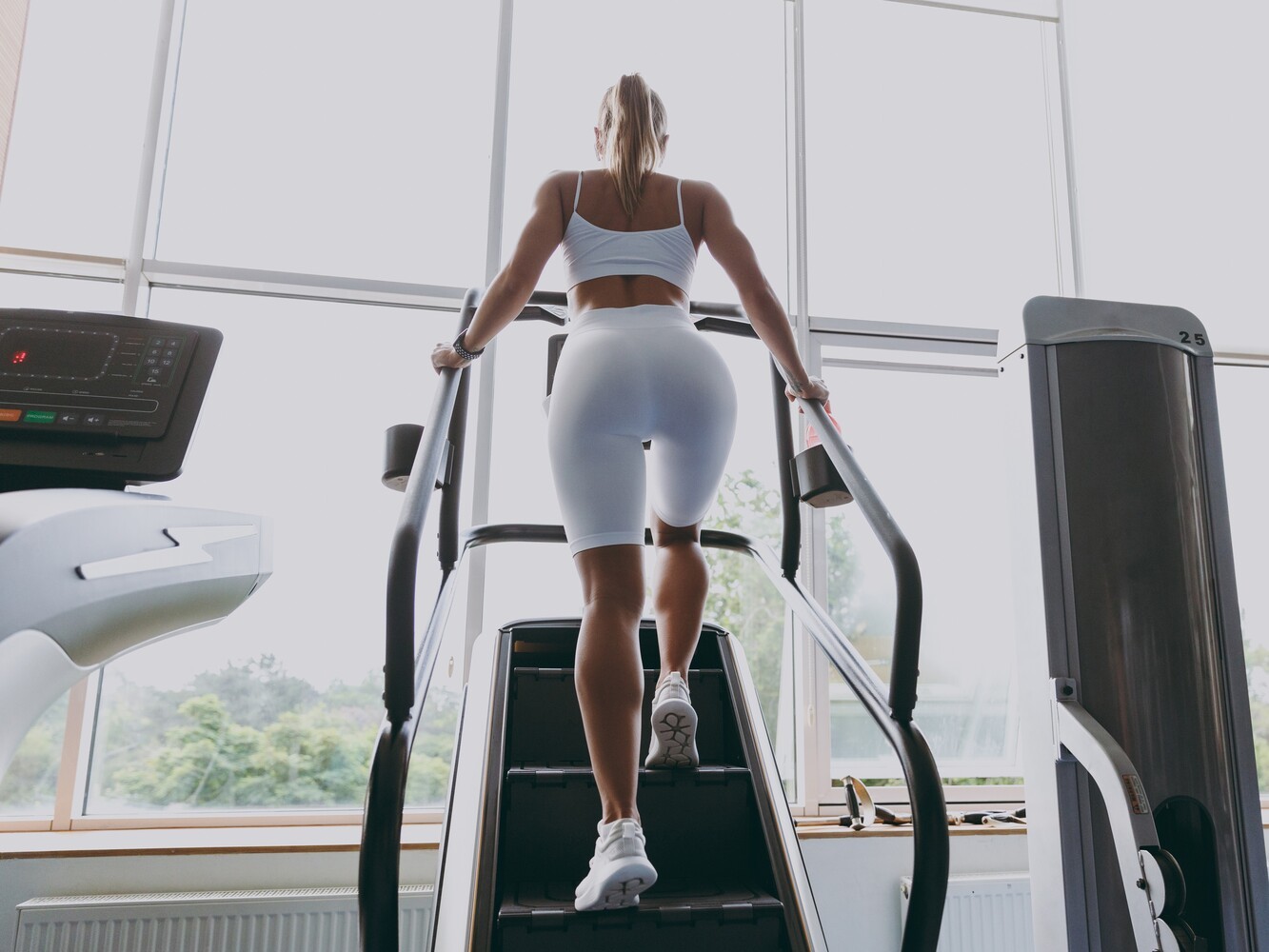 woman in white fitness gear doing a stair climber workout for weight loss in a gym with lots of natural light
